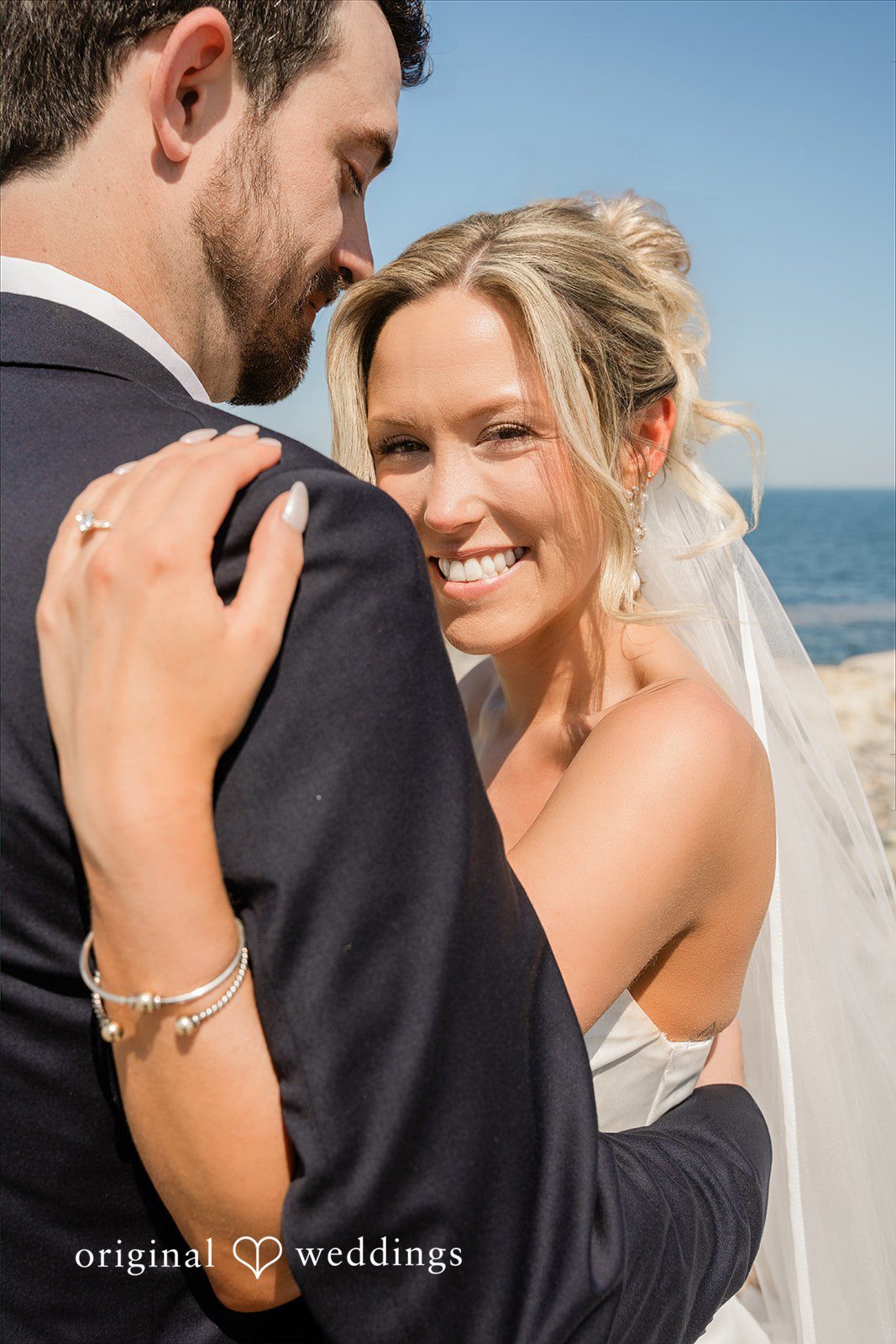 Jessica + Keegan A bride laughing joyfully while embracing her groom by the ocean.