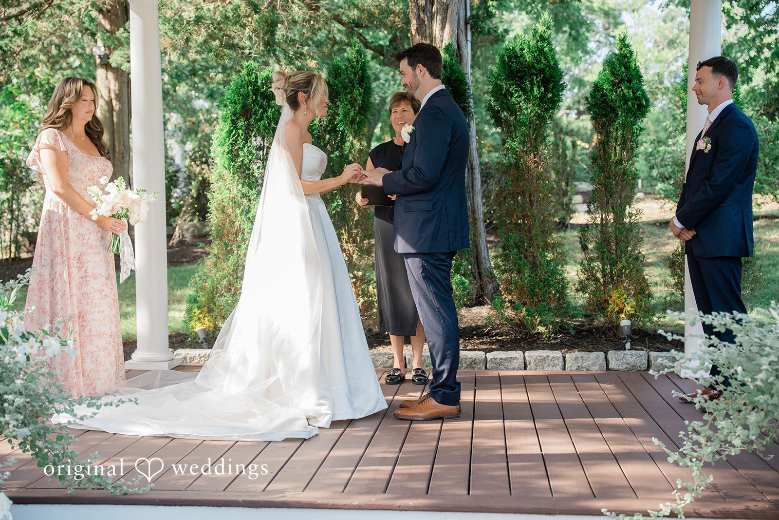 Jessica + Keegan A bride and groom standing at the altar under a floral arbor during a sunny ceremony.