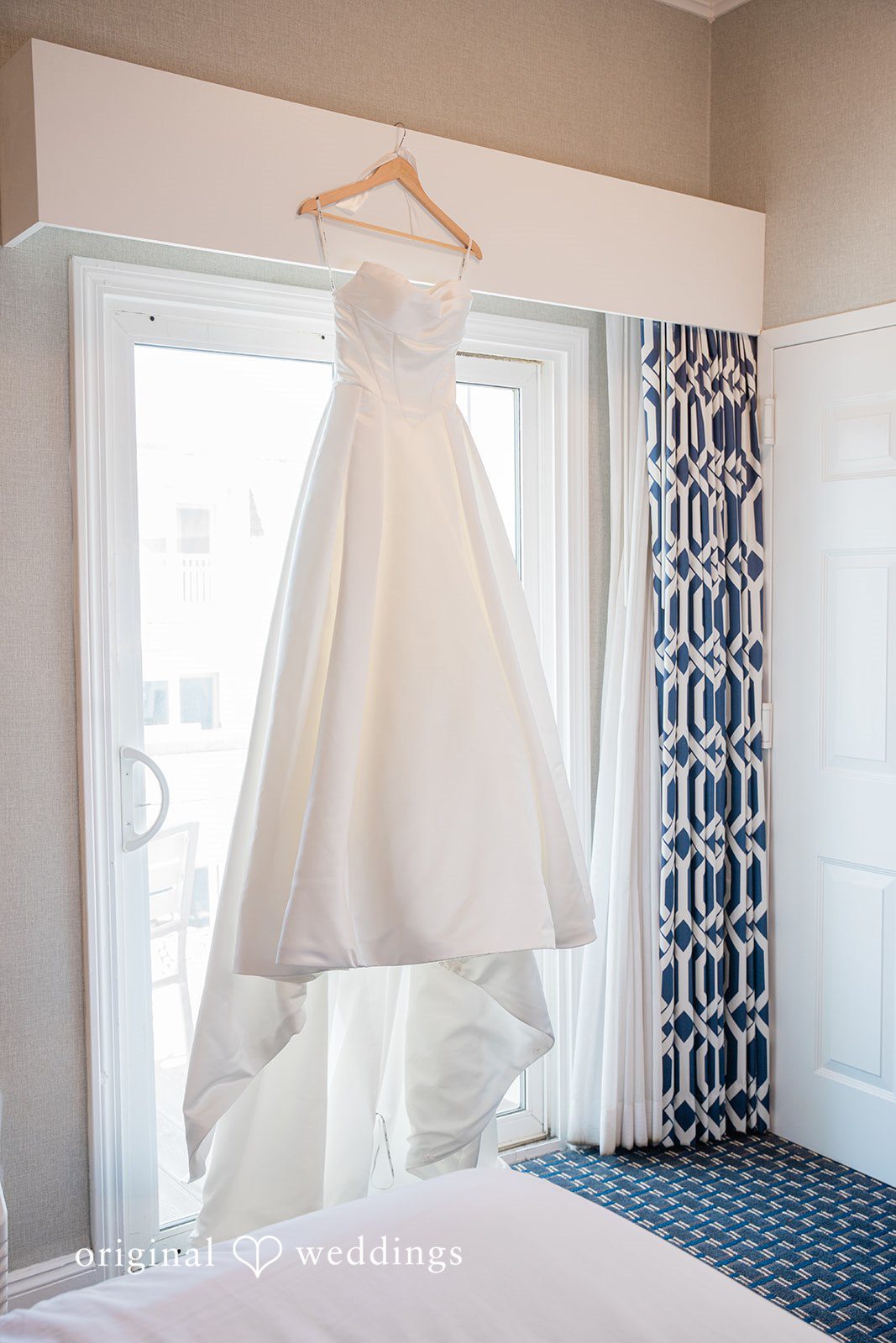 Jessica + Keegan A beautiful white wedding gown hanging elegantly in front of a window before the ceremony.