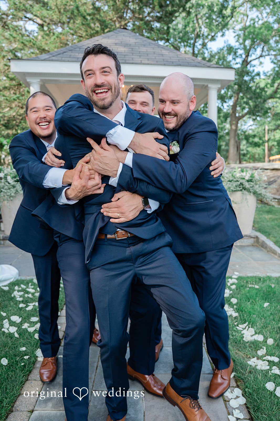 Jessica + Keegan A group of groomsmen playfully lifting and hugging the groom in celebration.