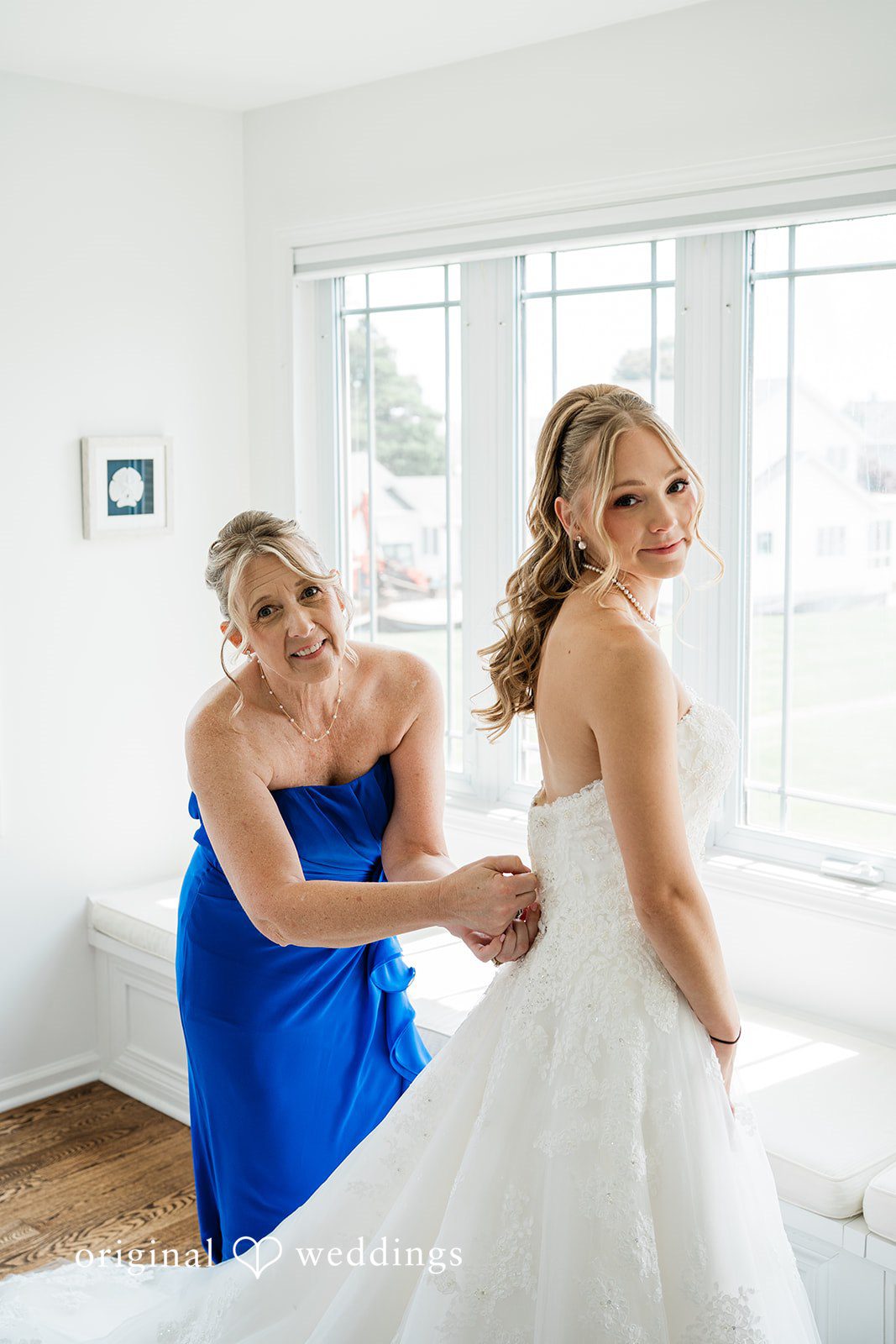 Veronica + Wyatt A bridesmaid helping the bride adjust the back of her white wedding dress.