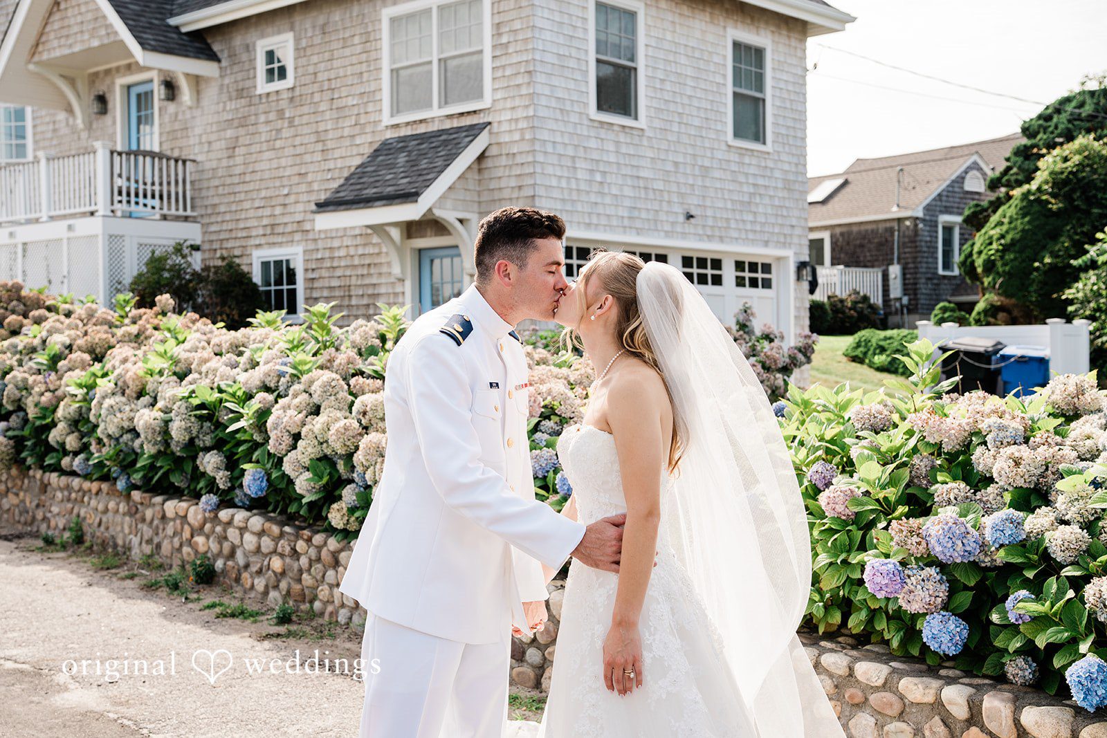 Veronica + Wyatt A bride and groom sharing a kiss next to green hedges.