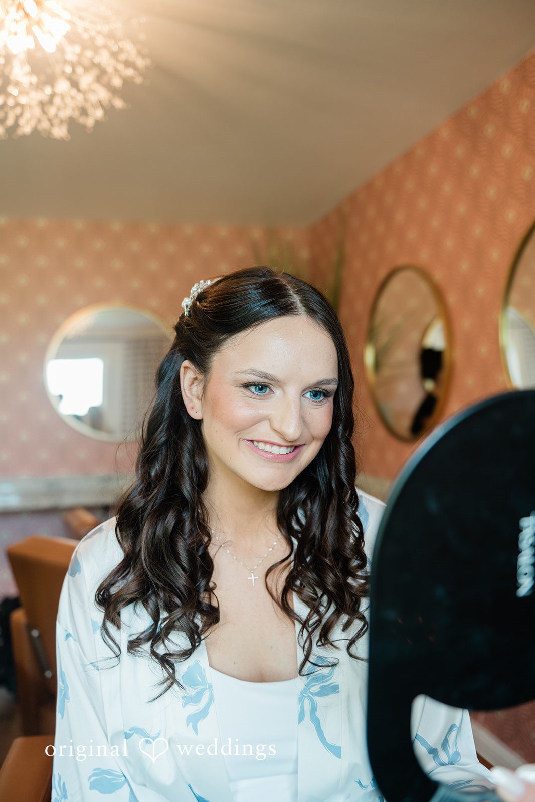 Paige + Stephen A smiling bride with dark hair and a detailed lace gown reflecting in a round mirror.
