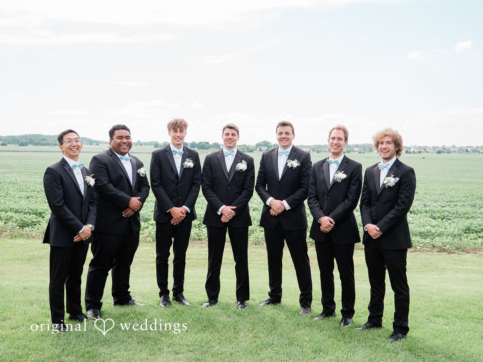Paige + Stephen A line of groomsmen in dark suits standing together in an open grassy field.