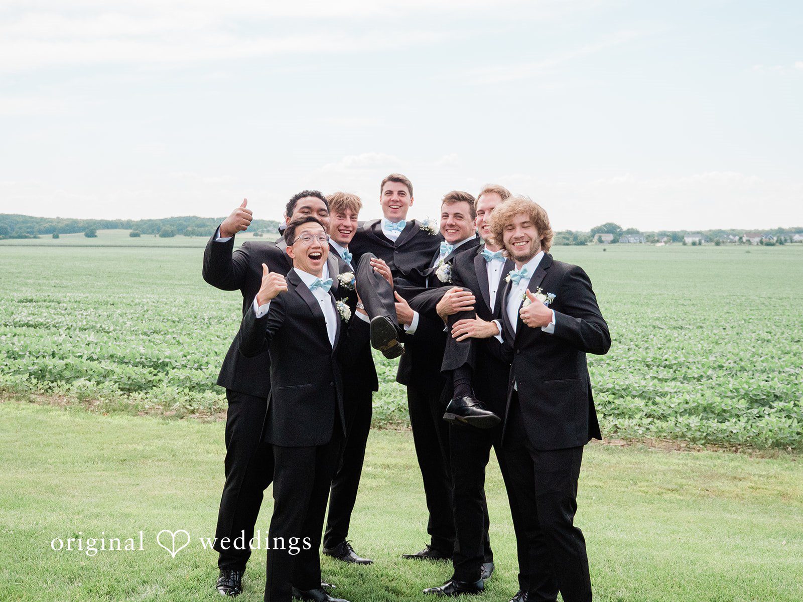 Paige + Stephen Groom and groomsmen in dark suits standing together and looking off to the side in a grassy field.