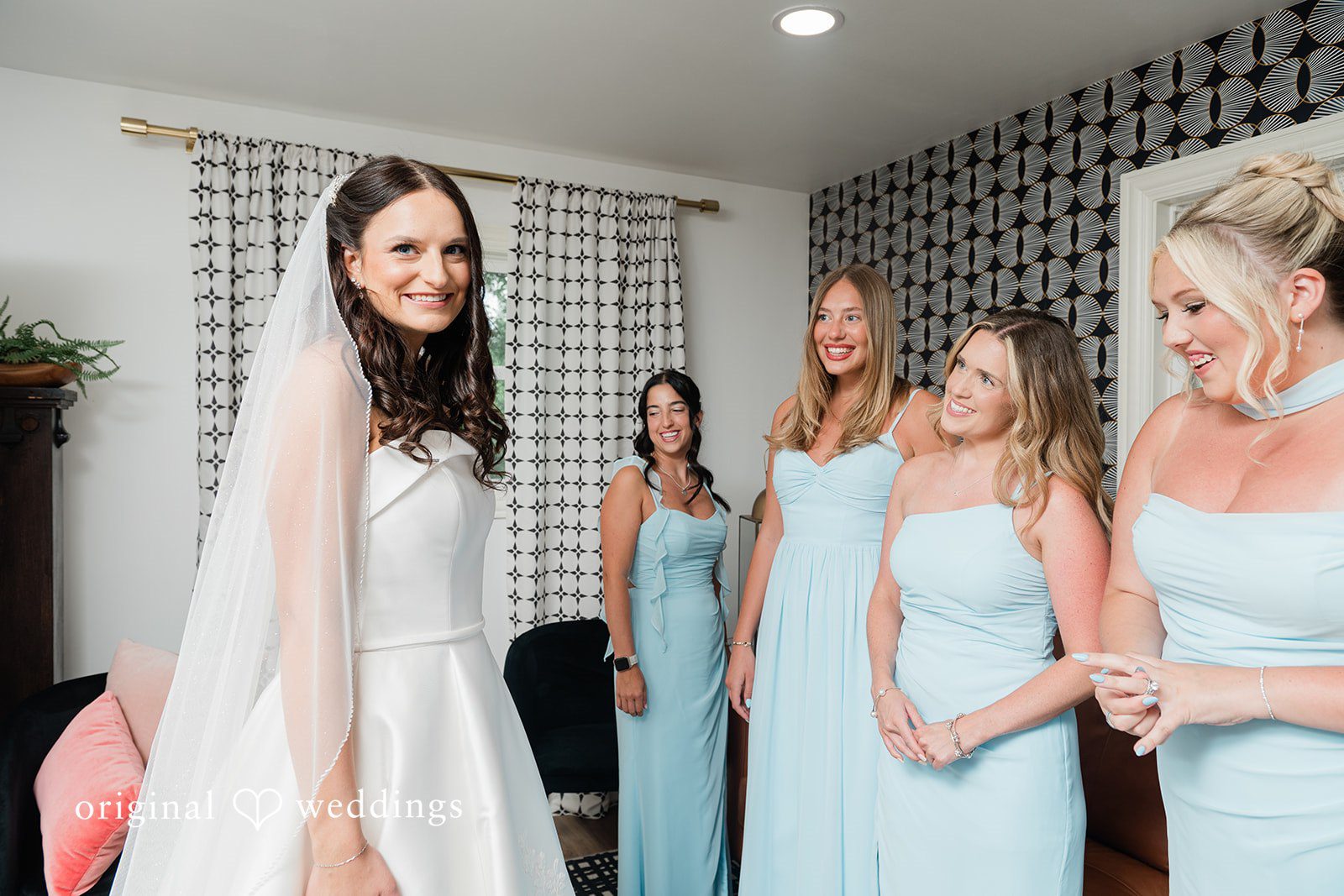 Paige + Stephen A bride in a long white dress standing next to bridesmaids wearing light blue gowns.