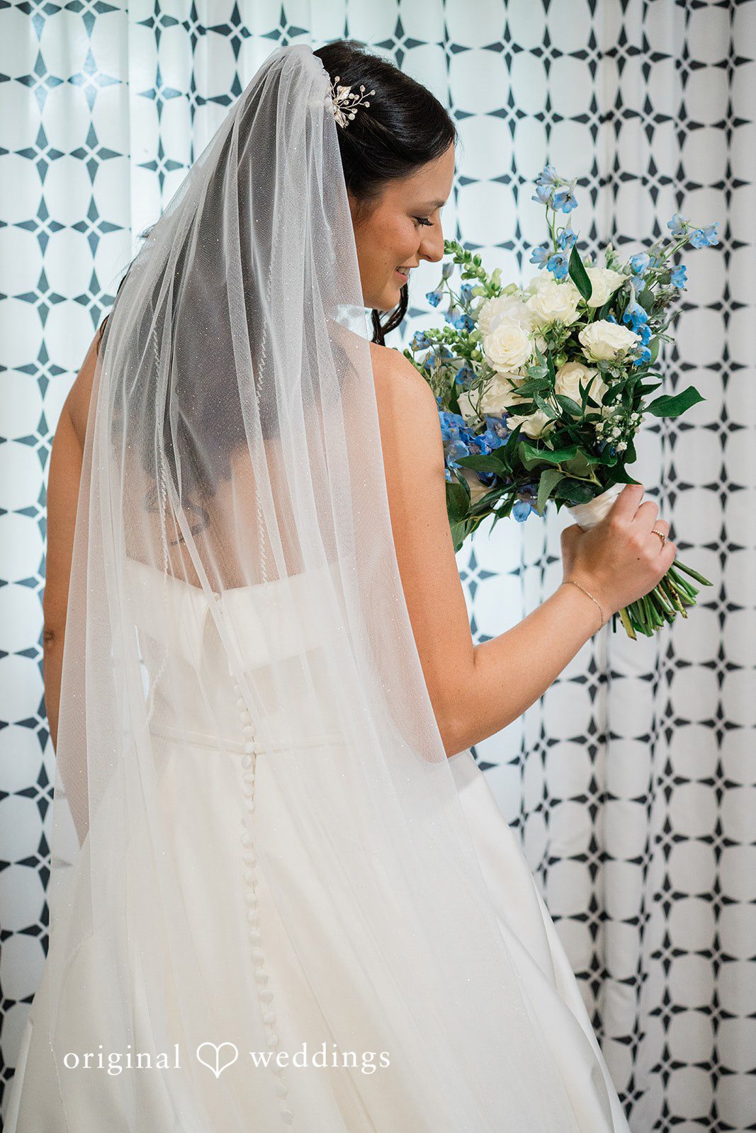 Paige + Stephen A bride in a white wedding gown holding a bouquet while looking over her shoulder against a pattern-tiled wall.