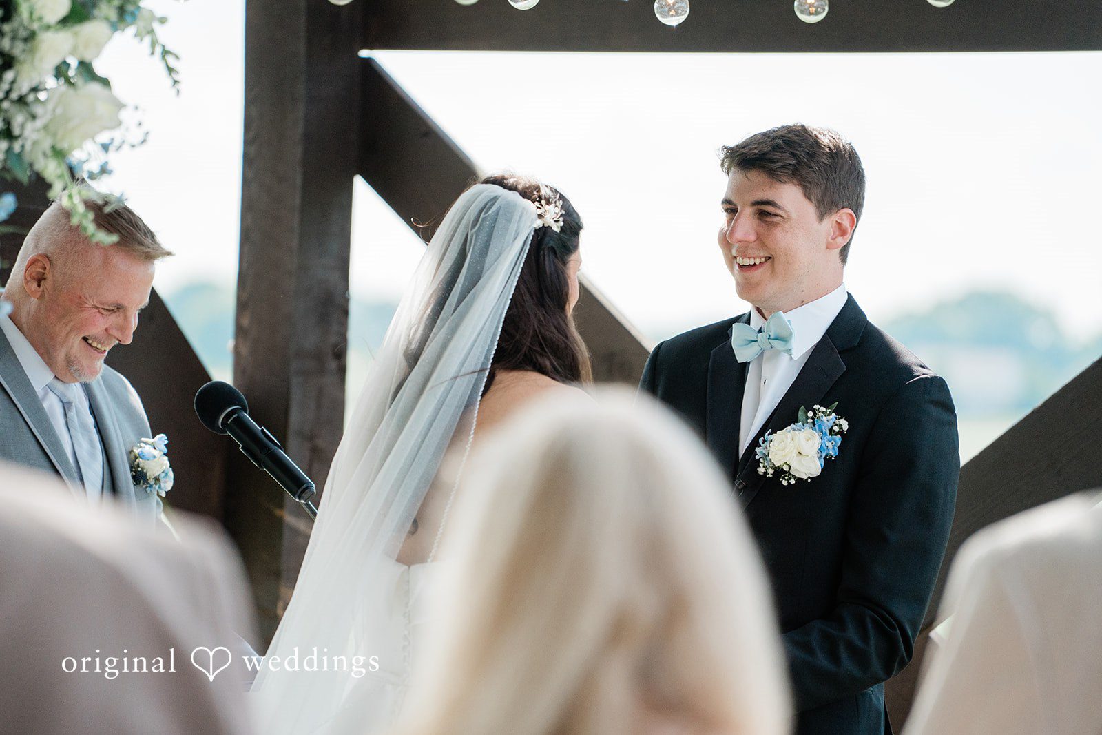 Paige + Stephen A groom in a black suit looking toward a blonde bride beneath a white ceremony veil.