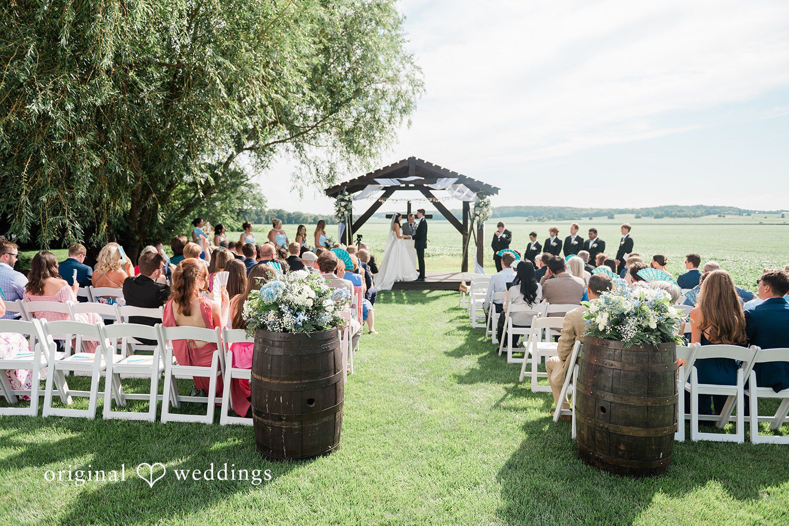 Paige + Stephen An open-air wedding ceremony setup with rows of white chairs leading to a wooden altar.