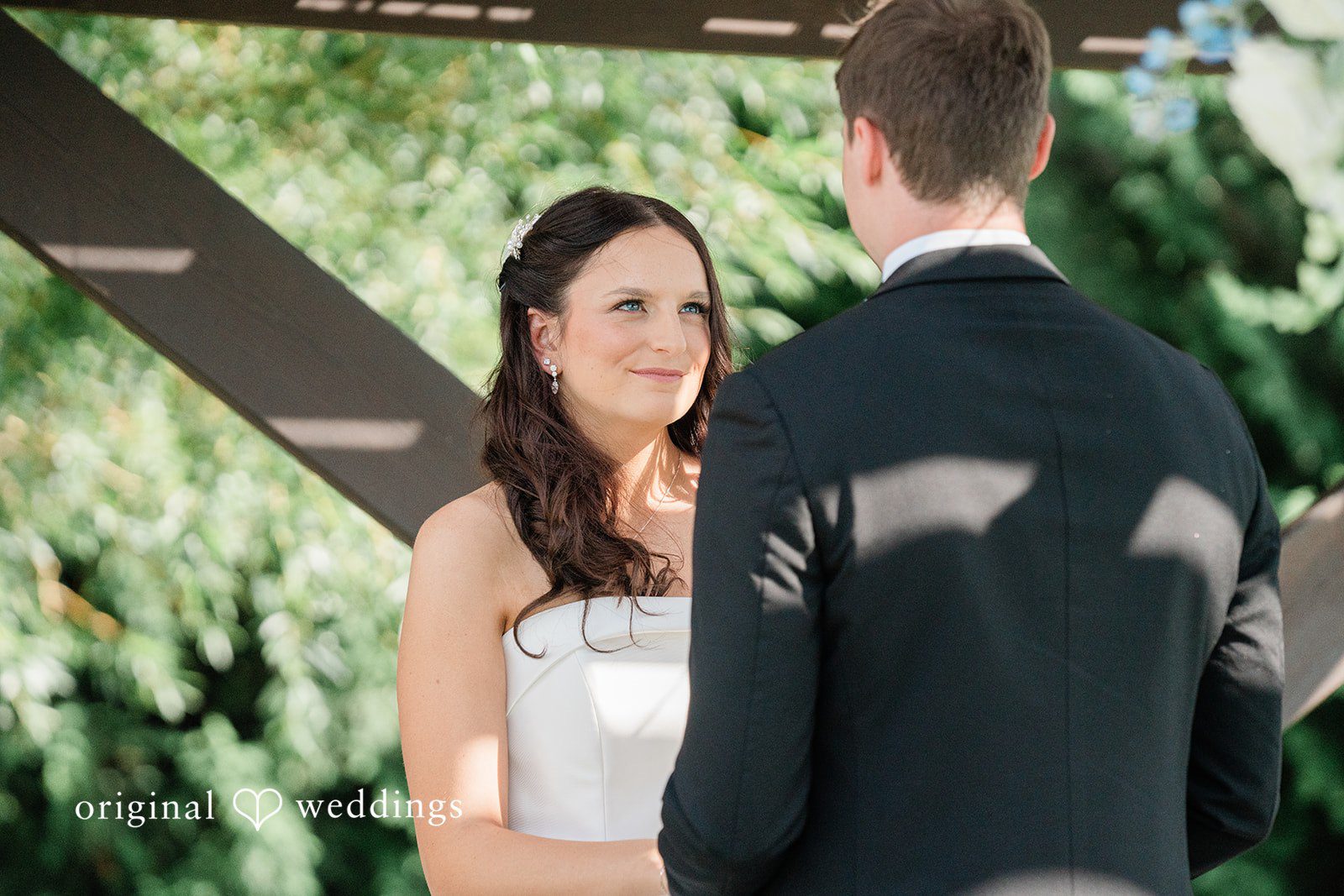 Paige + Stephen A bride with long dark hair smiling at a groom who has his back turned to the camera.