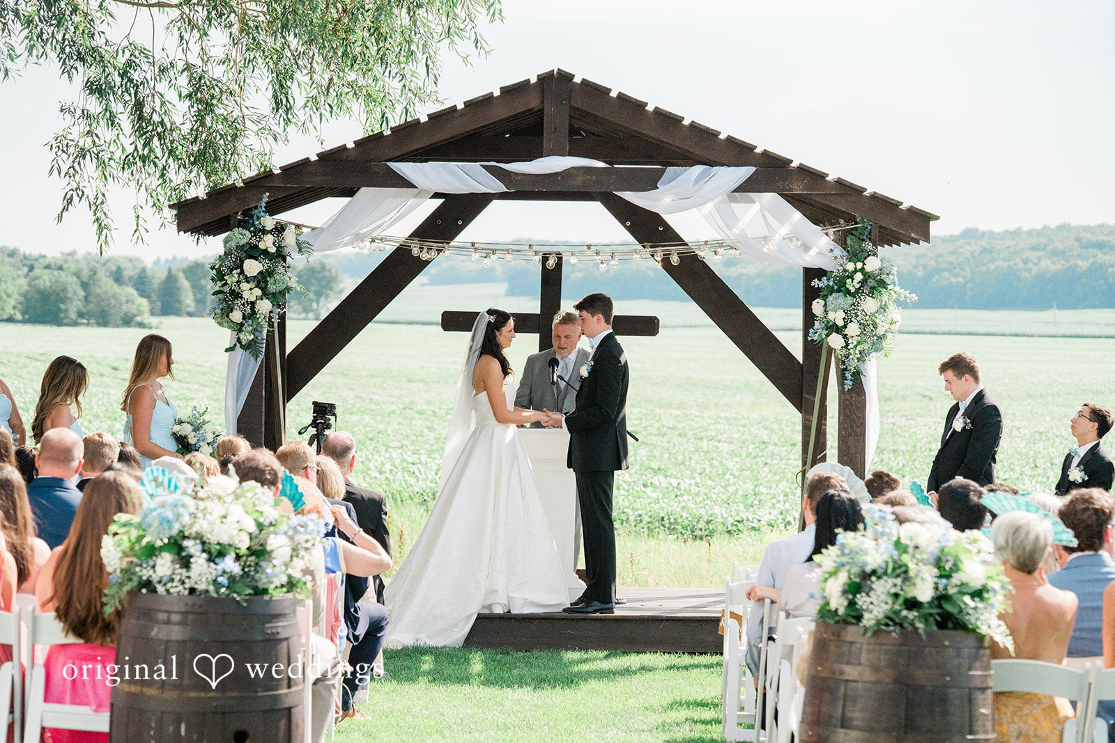 Paige + Stephen A wedding ceremony taking place under a rustic wooden pergola with guests seated on both sides.
