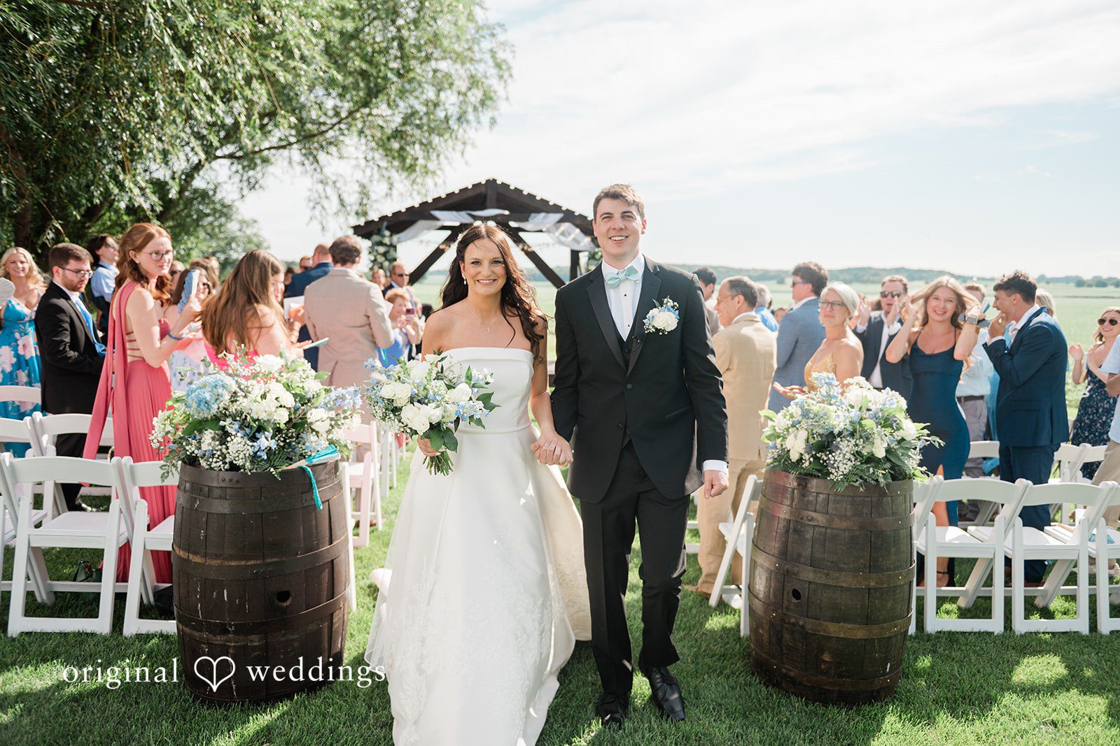 Paige + Stephen A bride walking down a grassy aisle between white chairs toward the groom.