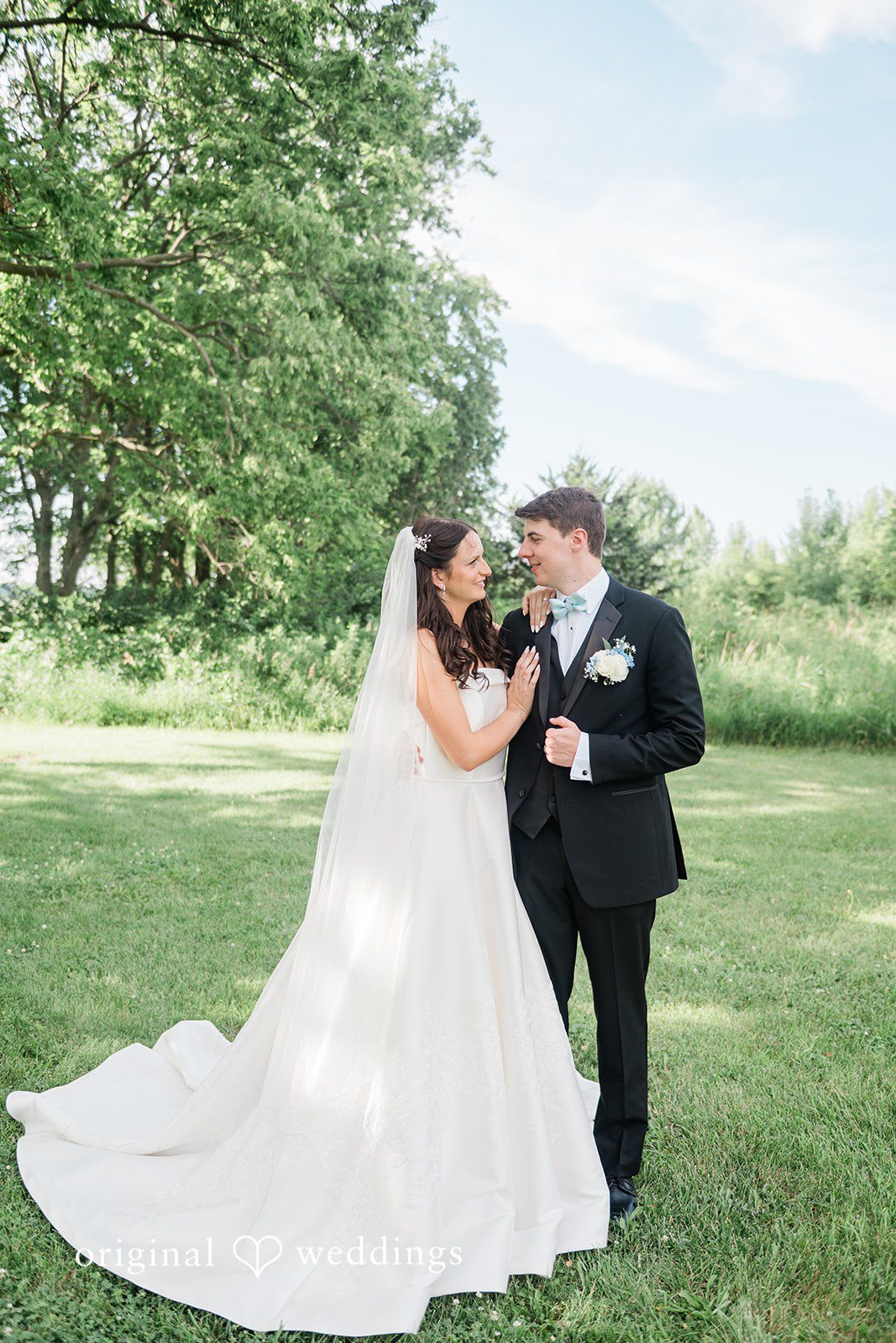 Paige + Stephen A bride and groom walking together across a sunny green field during their wedding day.