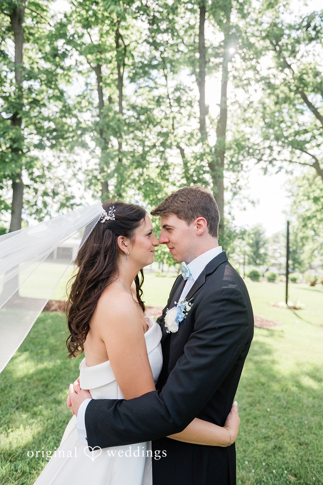 Paige + Stephen A groom wrapping his arms around a smiling bride from behind in a grassy park.