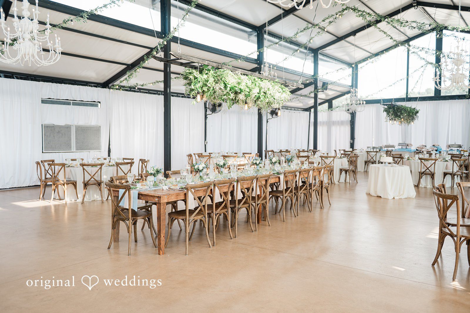 Paige + Stephen A long wooden dining table set for a wedding reception inside a spacious hall with black structural frames.