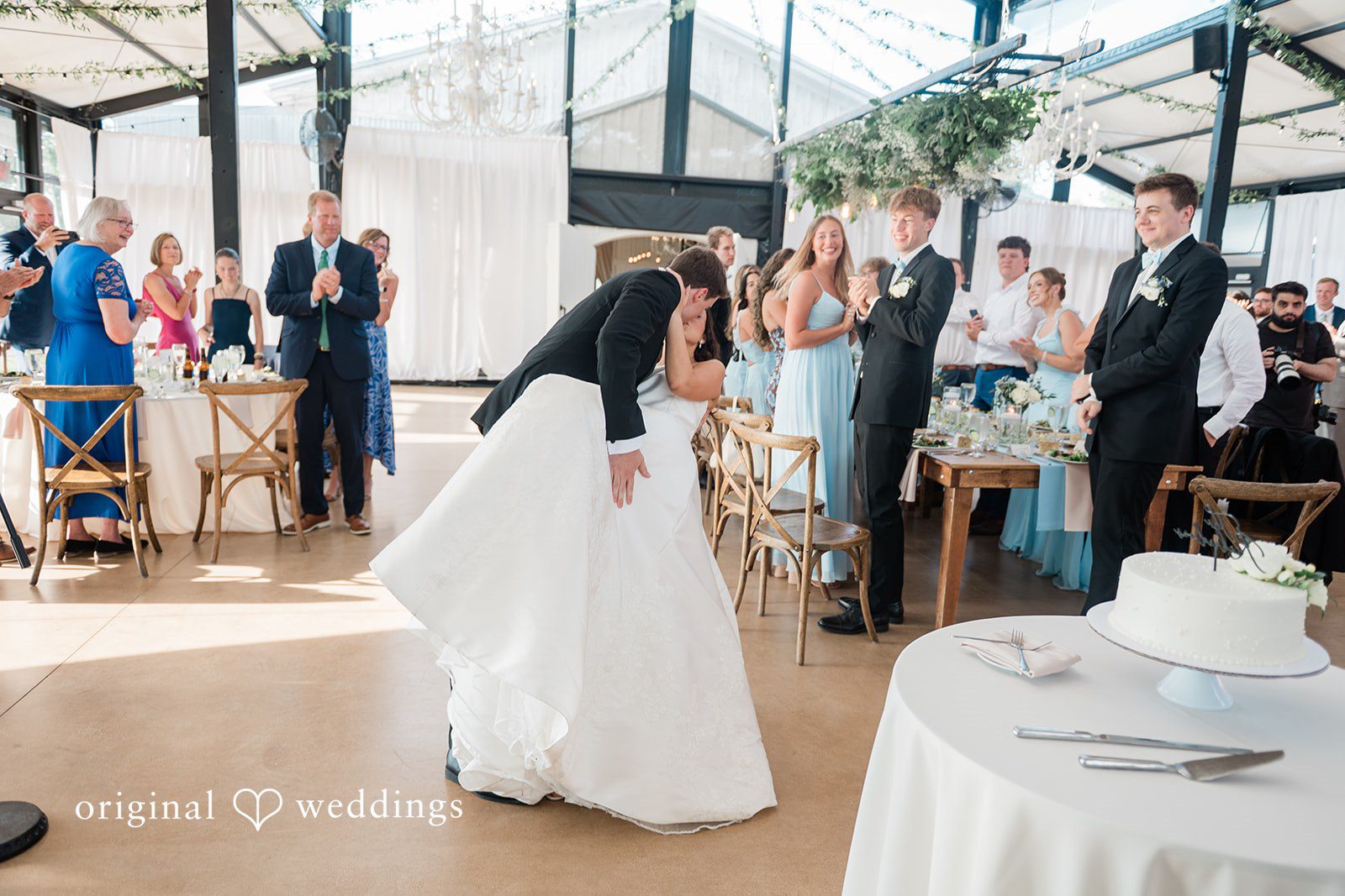 Paige + Stephen A bride in a white gown walking through a reception room filled with wedding guests.