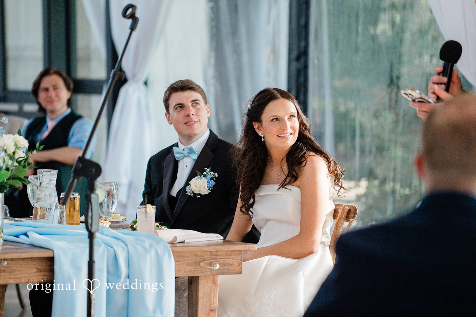 Paige + Stephen Wedding guests seated at a long reception table while a man speaks into a microphone.