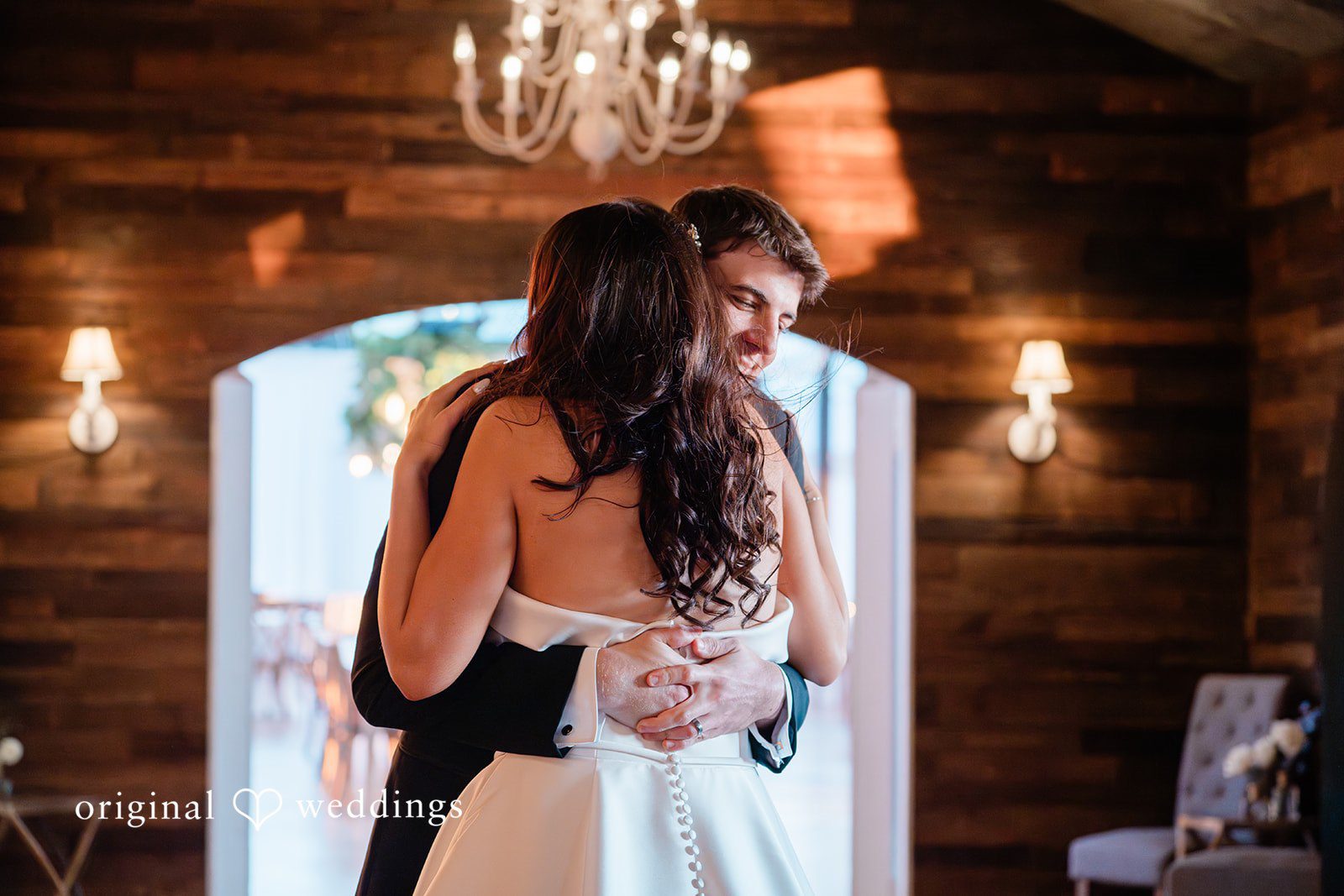 Paige + Stephen A groom embracing a dark-haired bride in front of a brightly lit arched doorway.