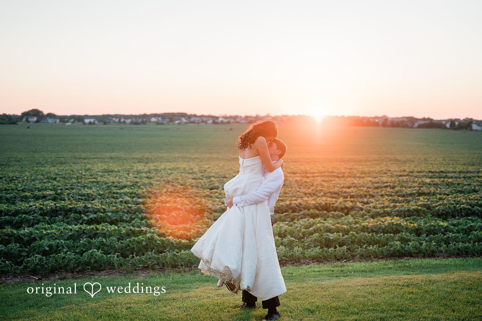 Paige + Stephen A bride in a white dress walking through a field during a golden hour sunset.