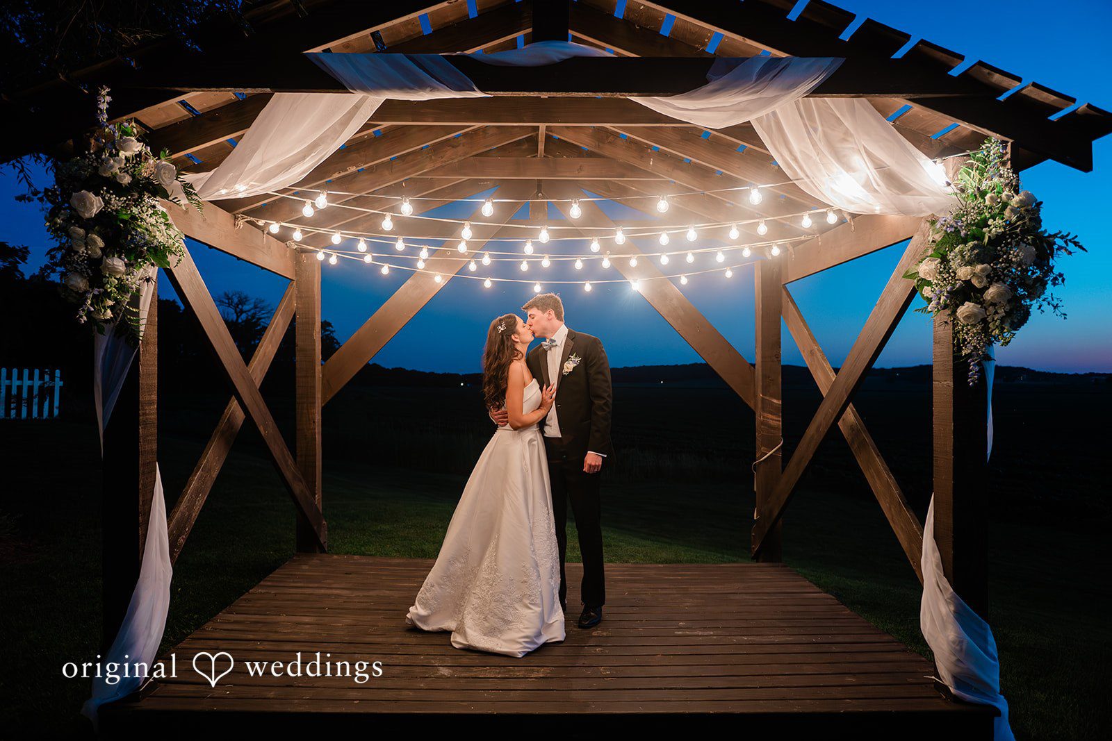 Paige + Stephen A bride and groom sharing a dance beneath an illuminated wooden structure at night.