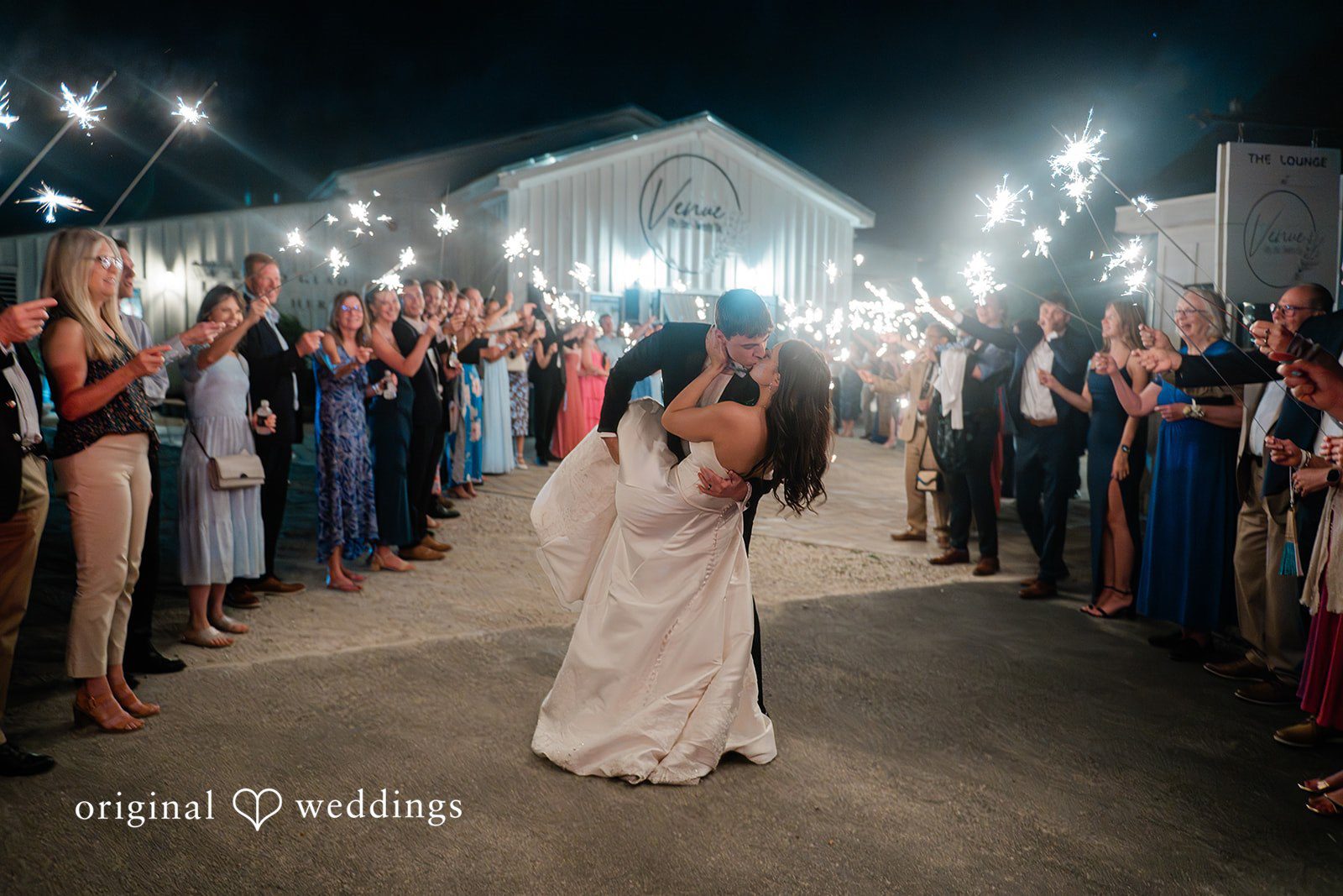 Paige + Stephen A bride and groom embracing and sharing a kiss during a sparkler send-off celebration.