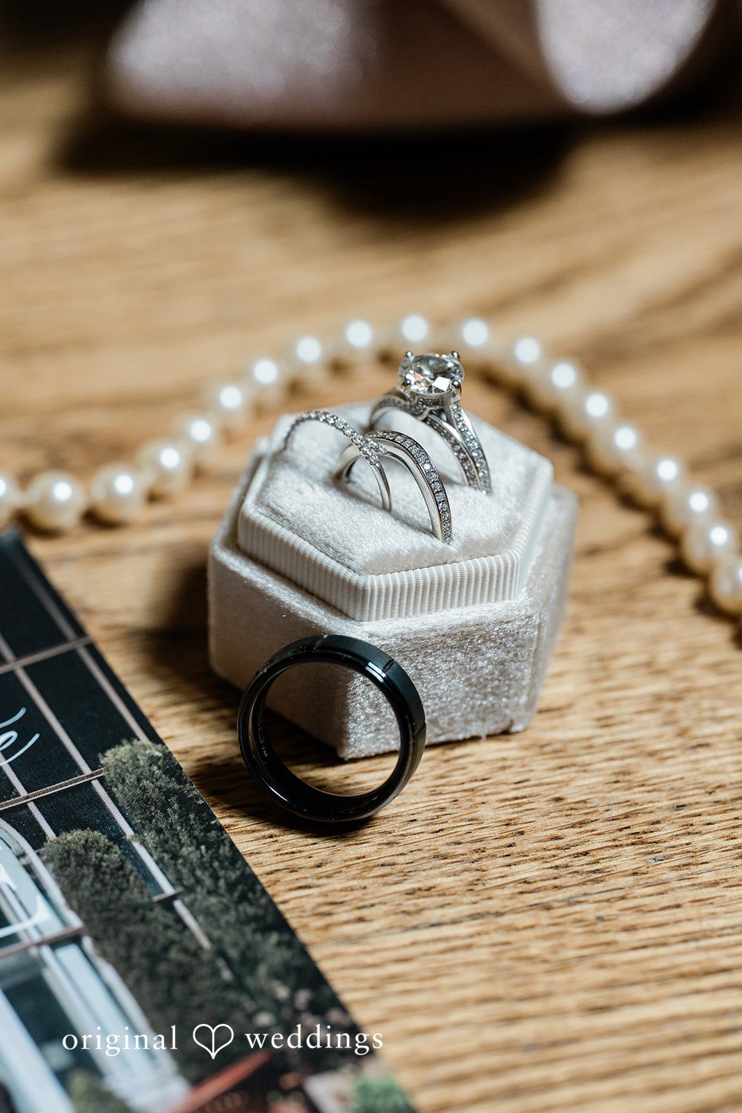 A close-up of wedding rings placed inside a small jewelry box next to a pearl necklace.