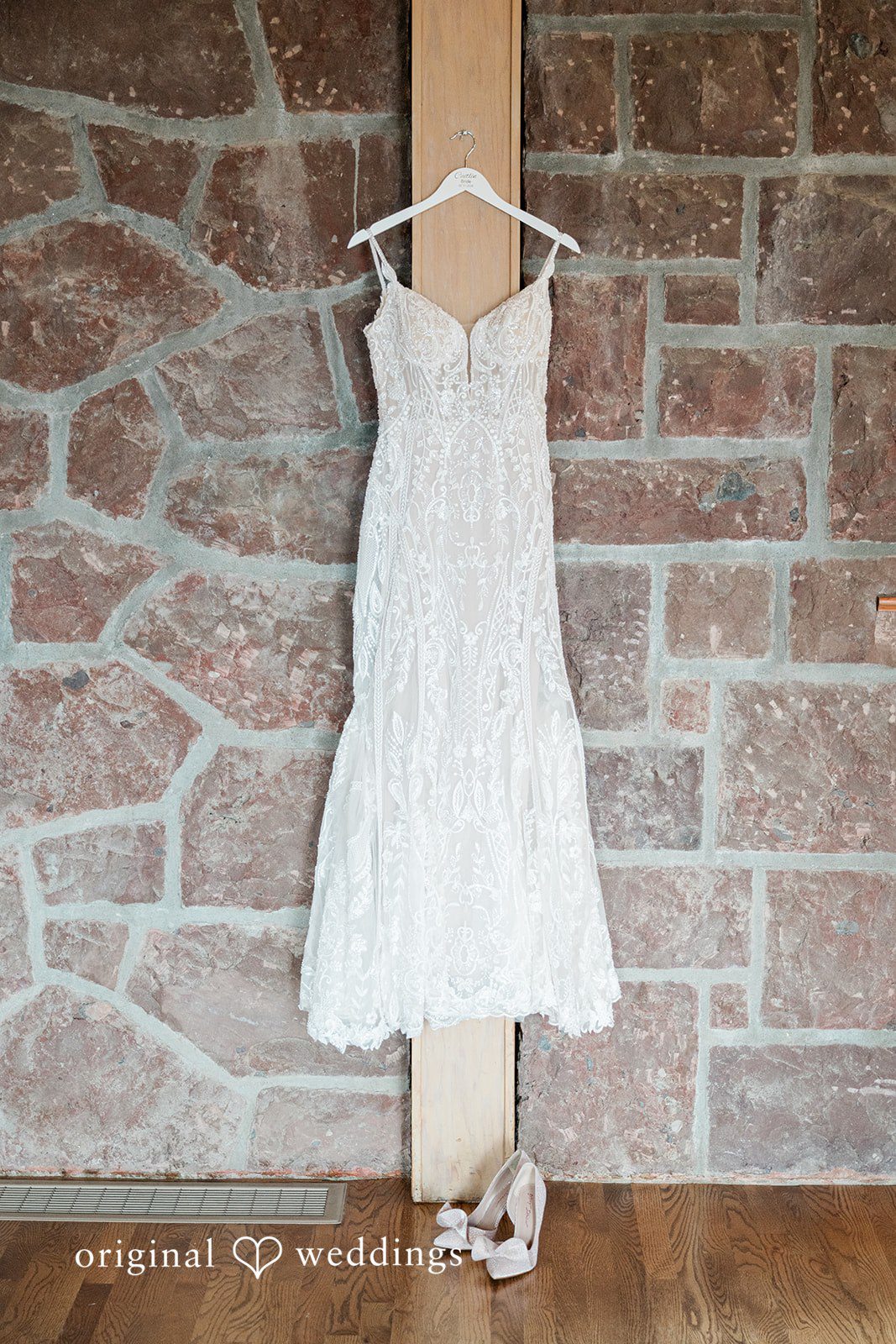A short white lace wedding dress hanging against a rustic stone wall.