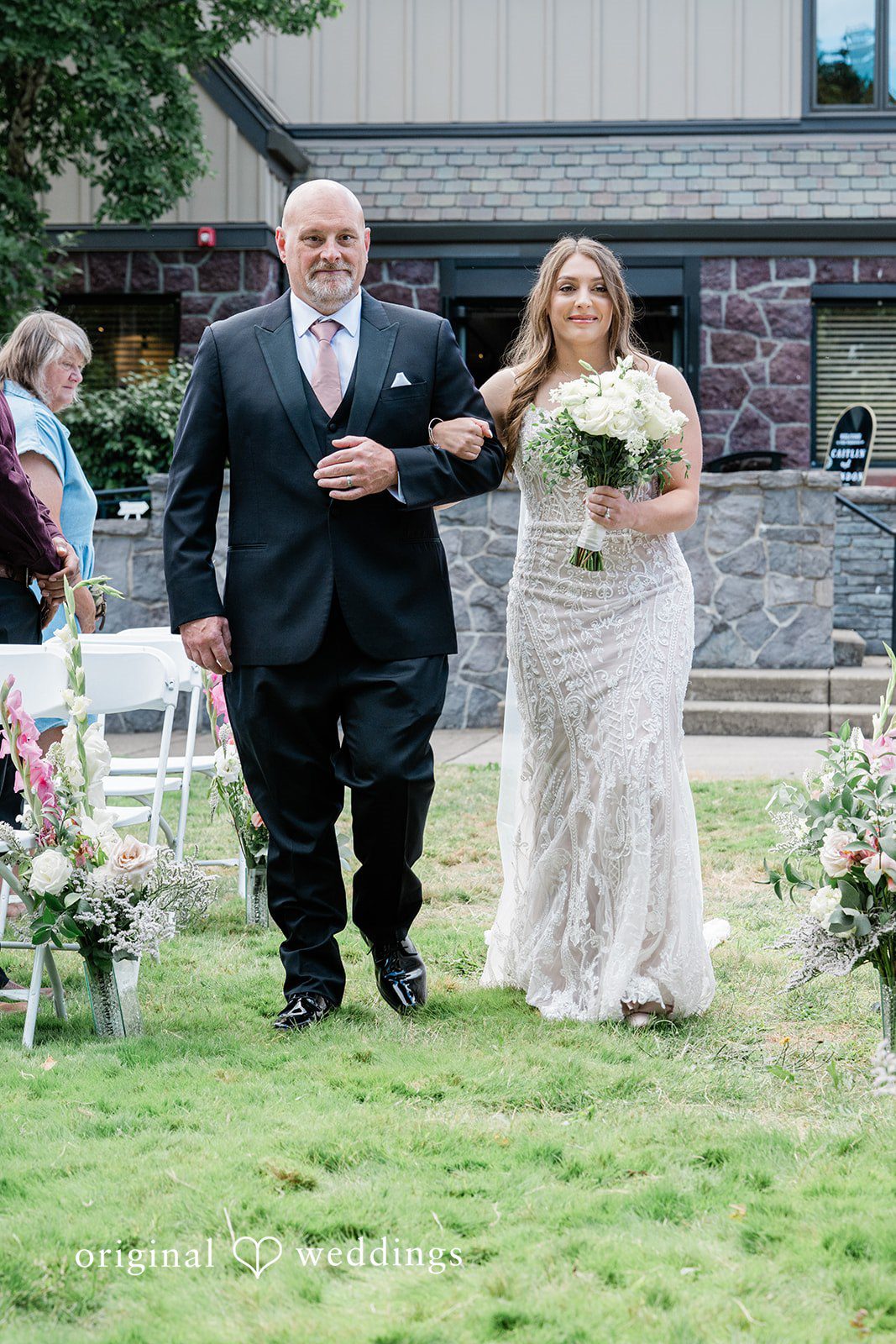 A bride and man walking down a grassy aisle.