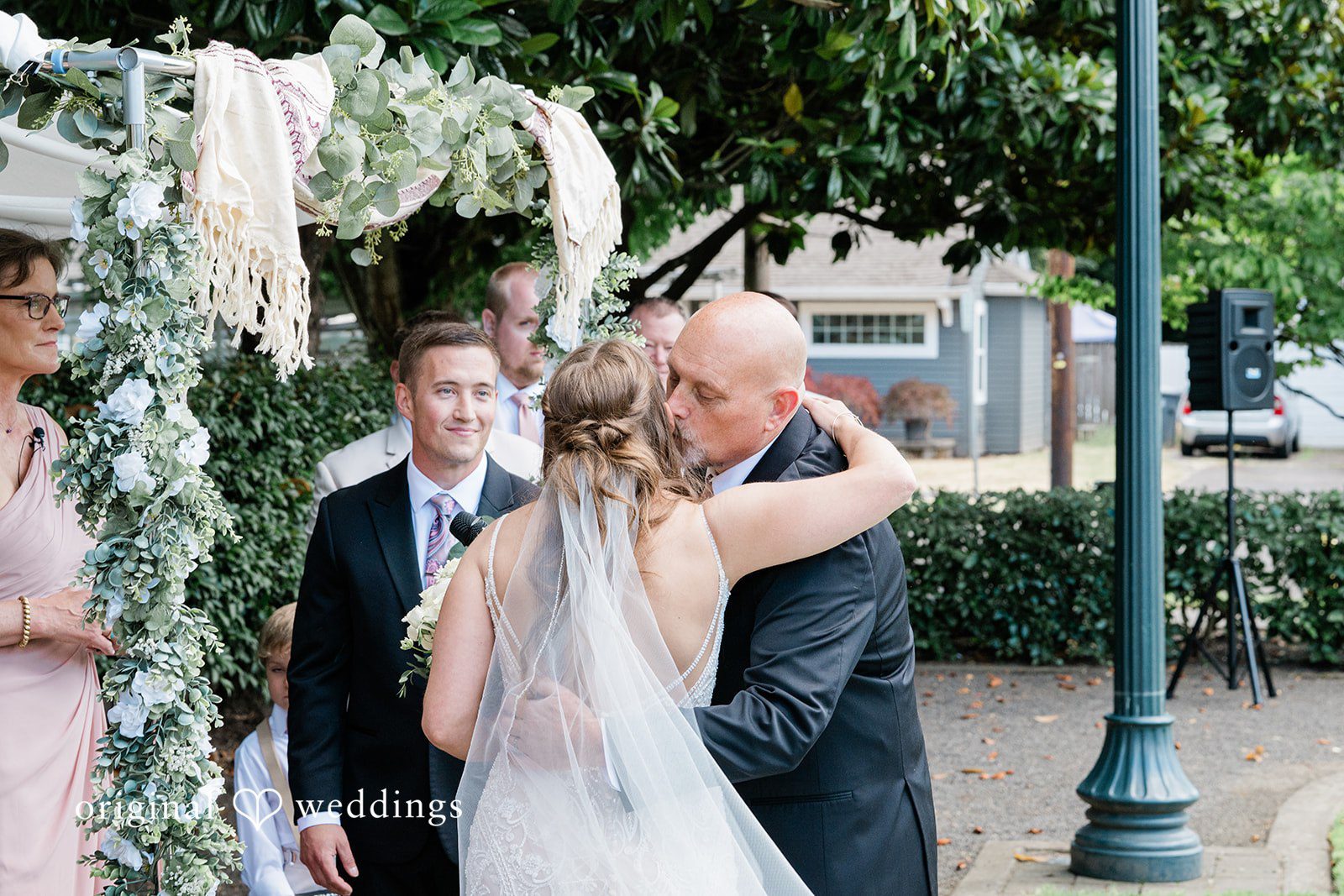 A bride sharing a close embrace under a leafy tree during their wedding.