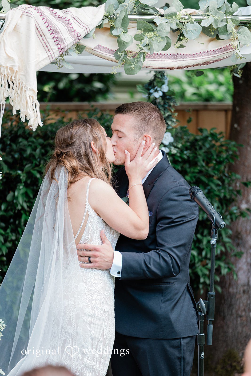 A bride and groom sharing a romantic kiss together under a floral arbor.