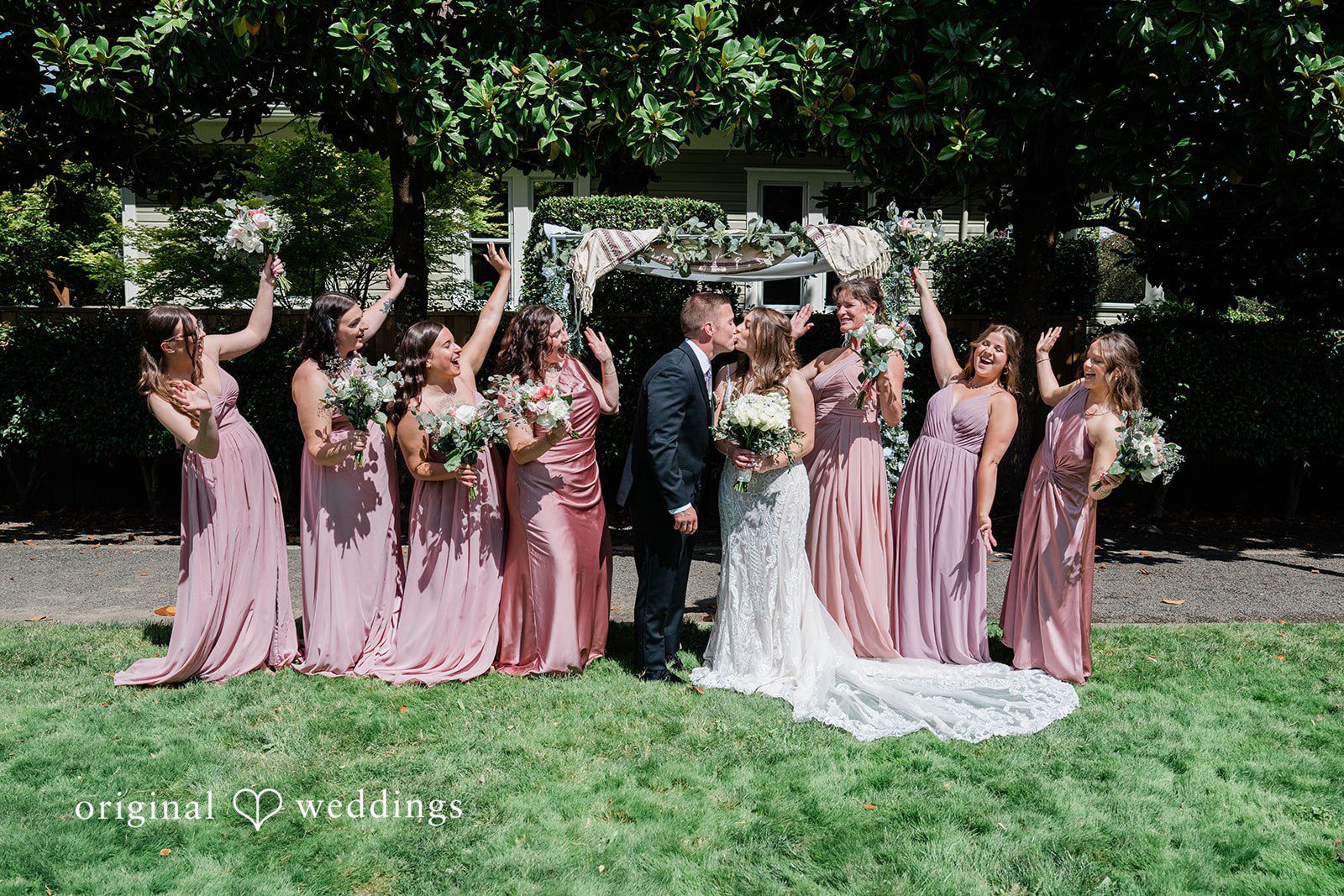 A large wedding party posing together in a line on a grassy lawn.