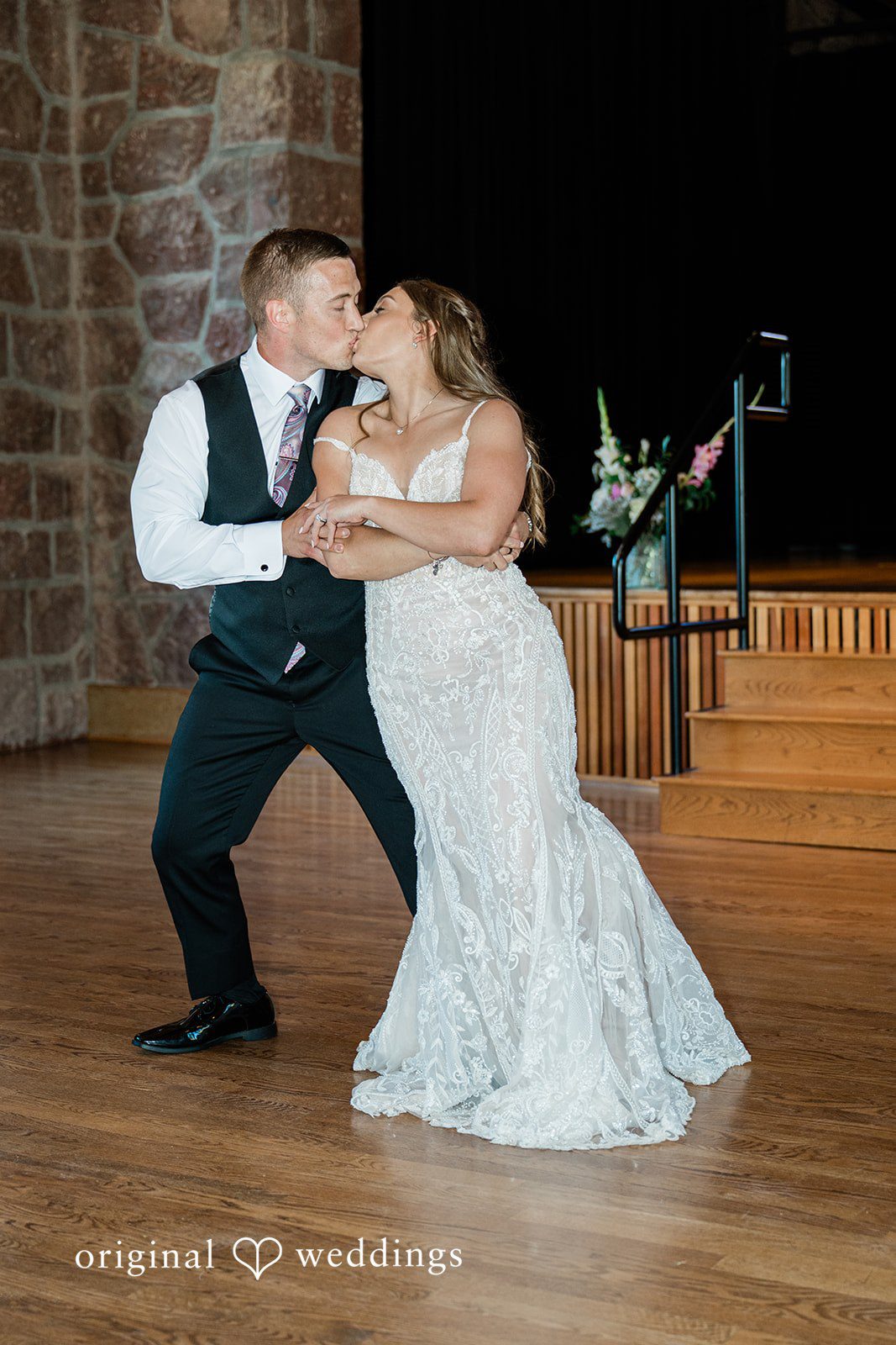 A bride and groom dancing together happily while guests watch in the background.