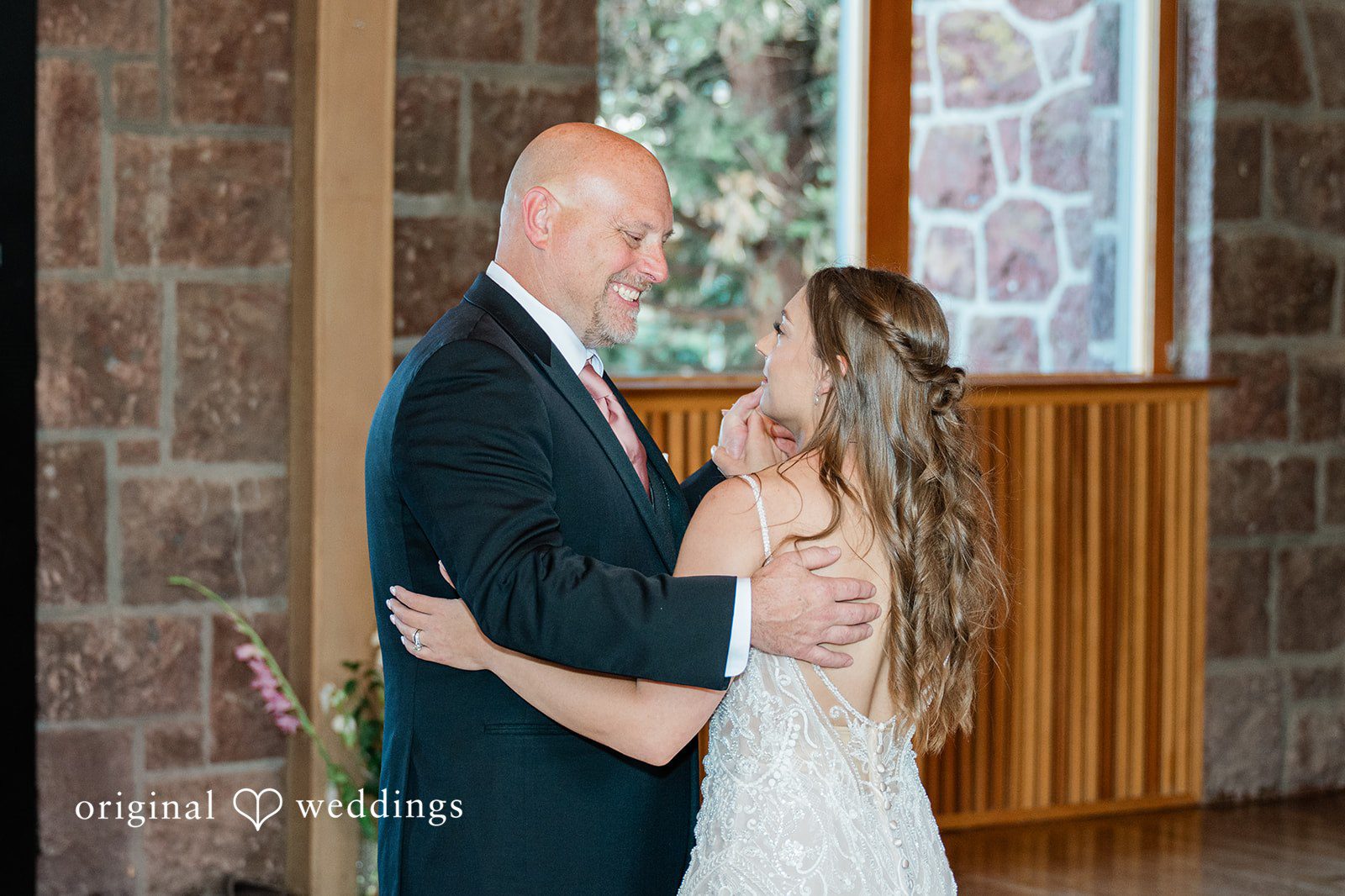 A man in a suit holding his bride close as they stand near a wooden wall.