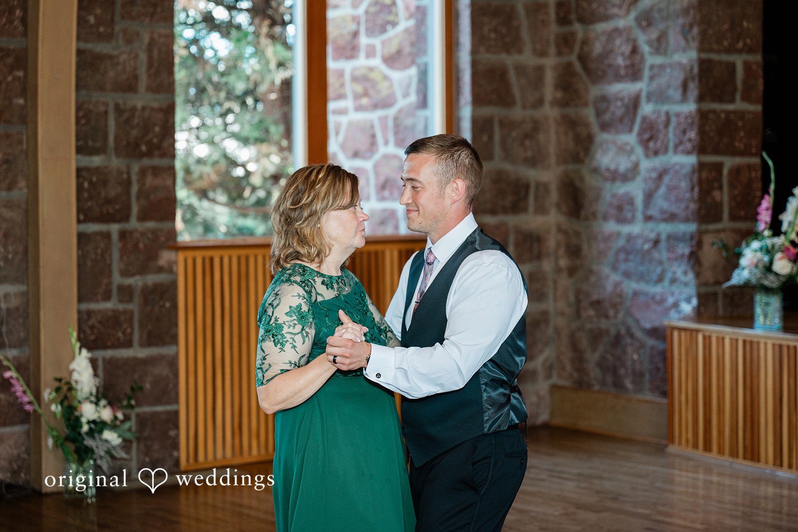 A groom standing with a women wearing a dark green dress inside a rustic room.