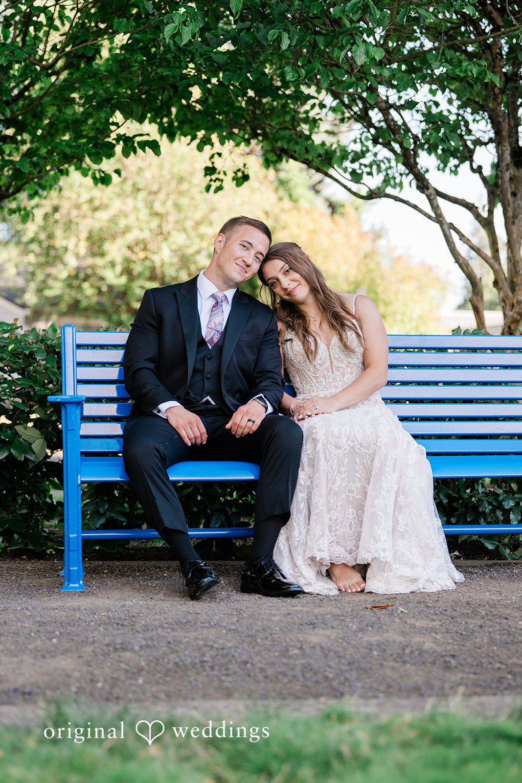 A bride and groom sitting closely together and smiling on a blue park bench.