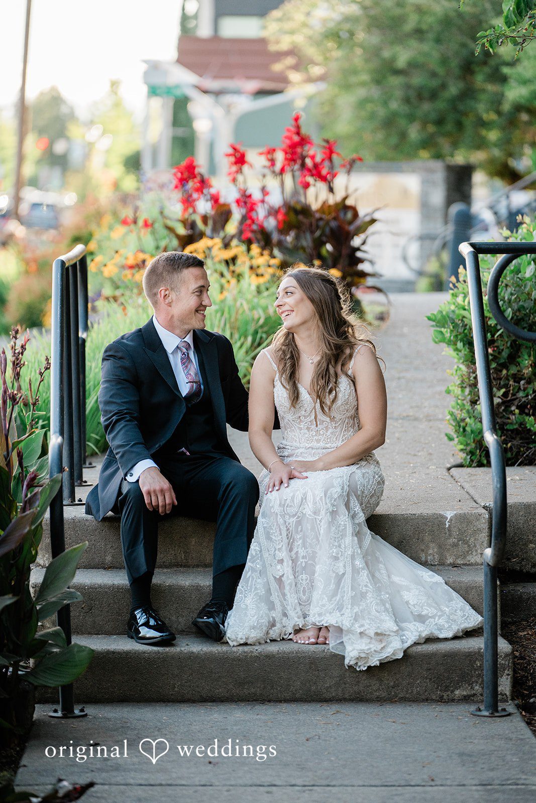 A bride and groom sitting together on concrete steps leading to a building.