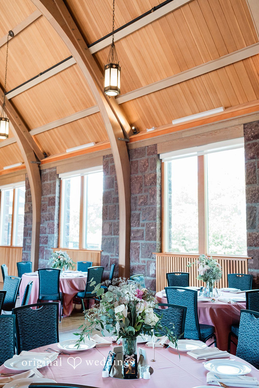 A bright reception room setup with rustic wooden pillars and teal table linens.