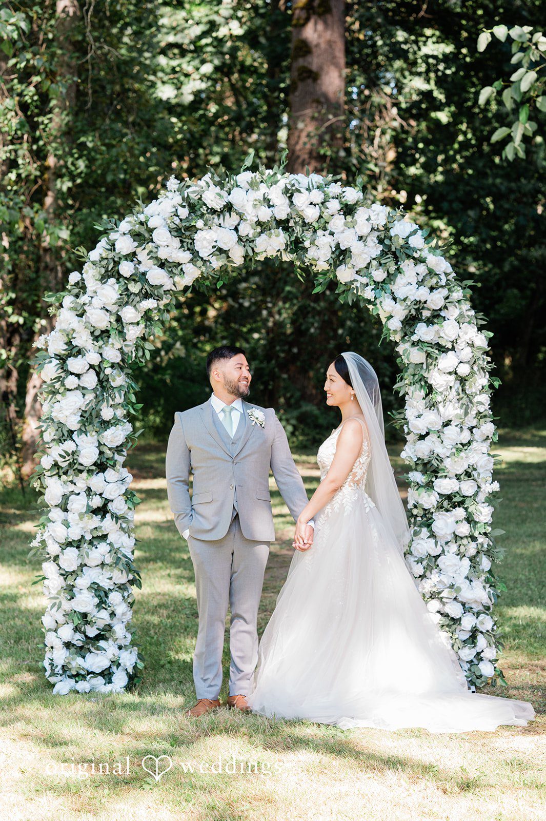 Harley + Mei A bride and groom facing each other in front of a wedding arch.