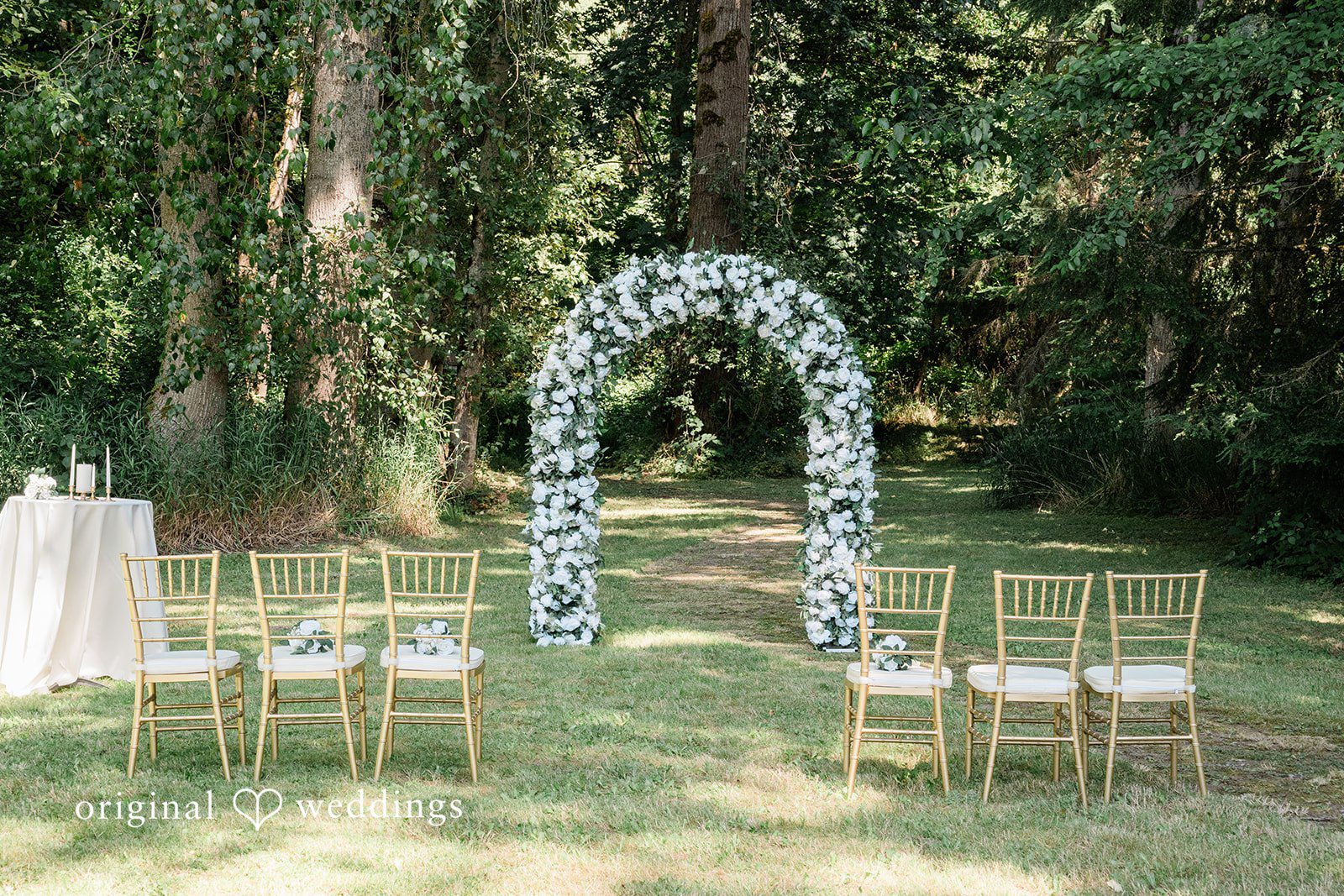 Harley + Mei An empty wedding altar decorated with white flowers set up in a grassy field.