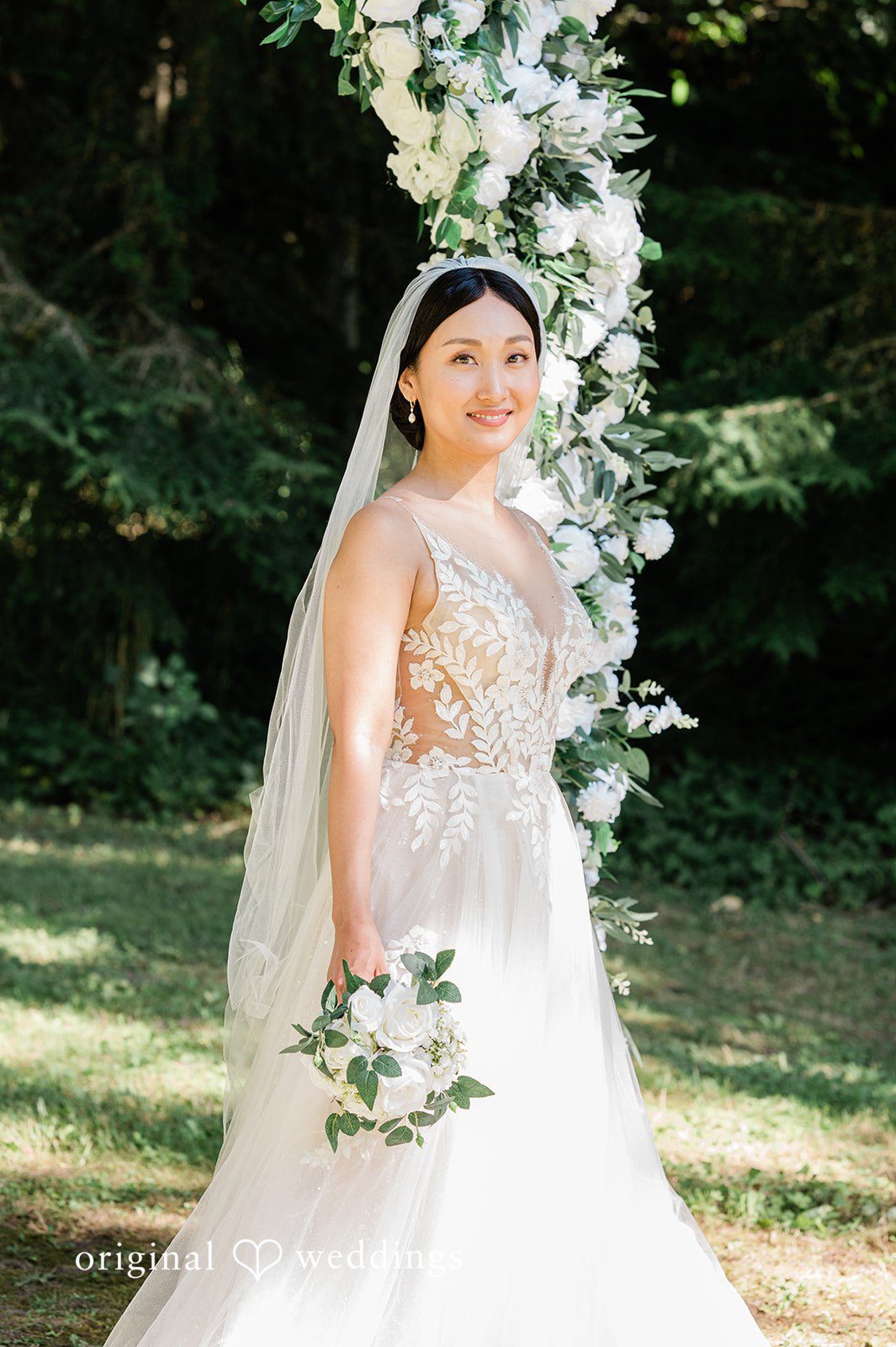 Harley + Mei A bride in a white gown walking and smiling while holding a bouquet.