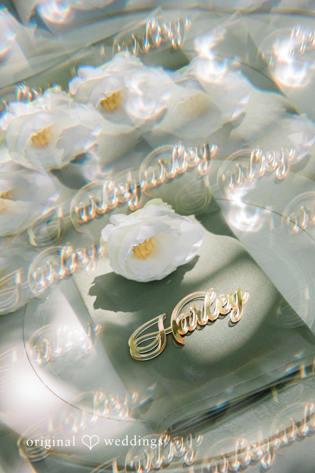 Harley + Mei Close-up of tableware with white plates, gold accents, and a clear card on a table.
