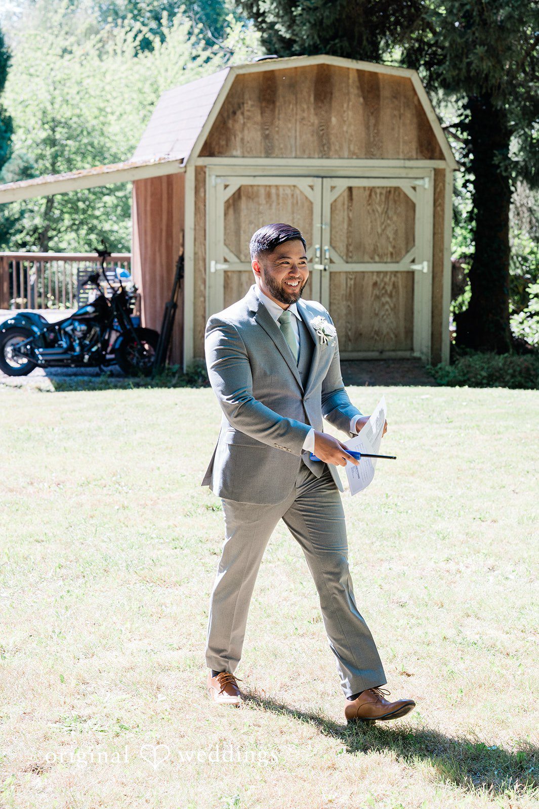 Harley + Mei A man dressed in a grey suit walking across a grassy field near a cabin.