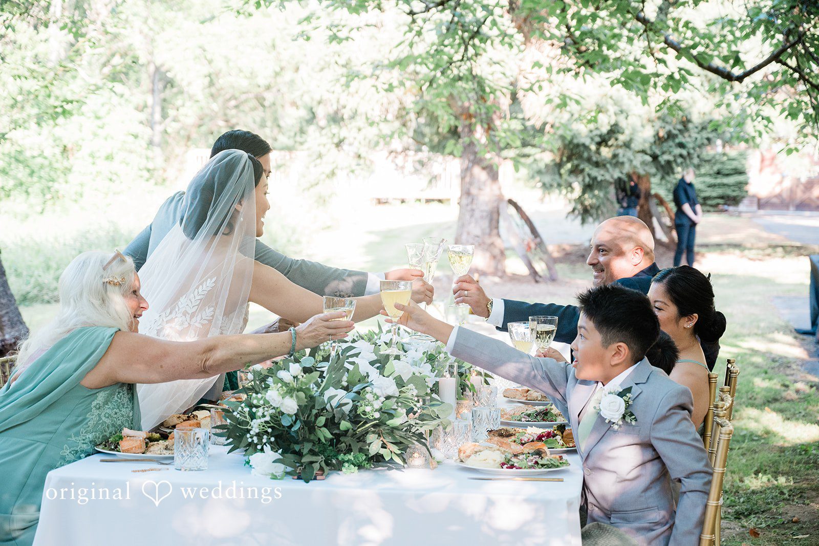 Harley + Mei A wedding reception toast with people raising their glasses around a table.