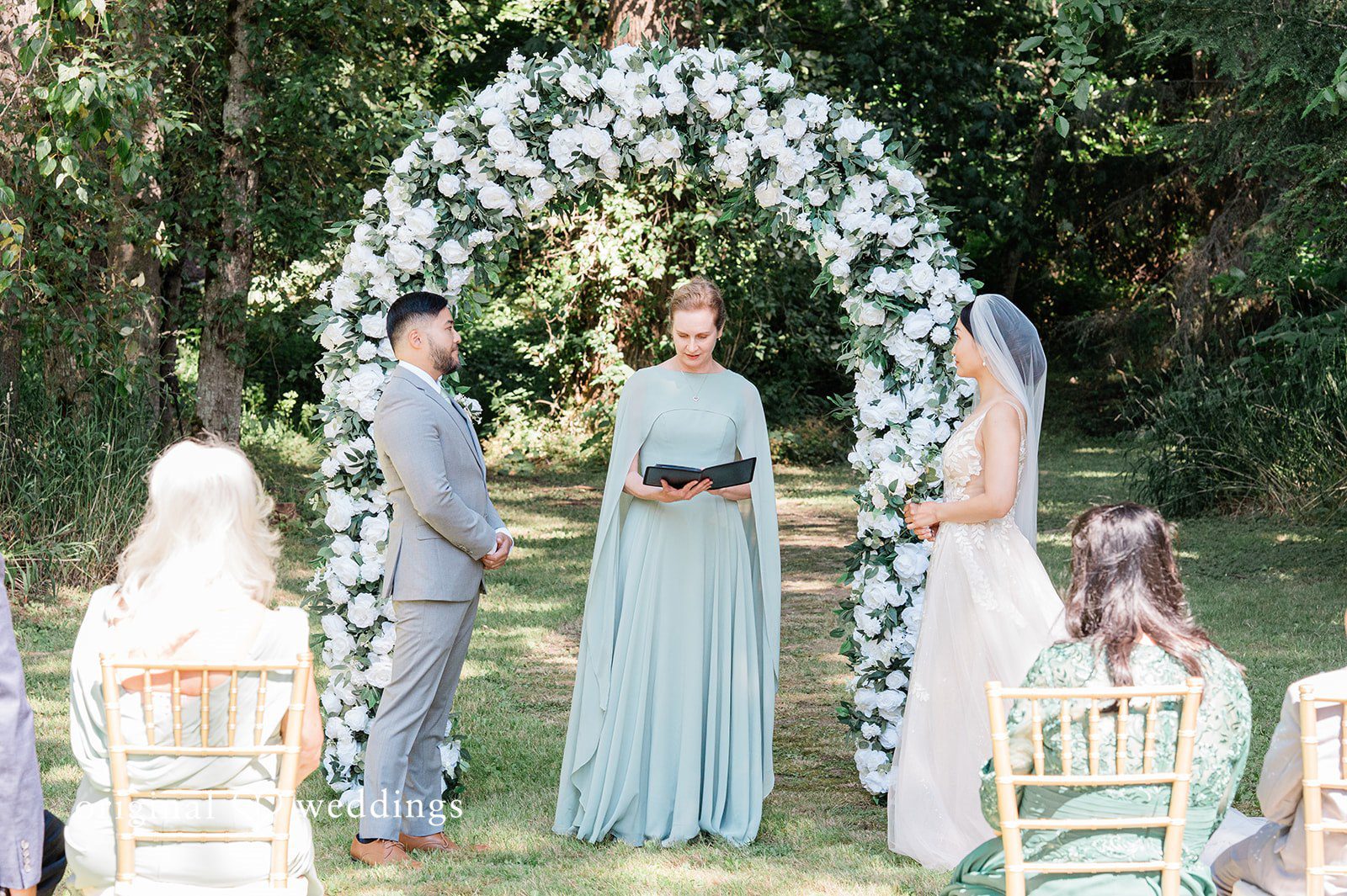 Harley + Mei A group of people standing beneath a floral wedding archway.