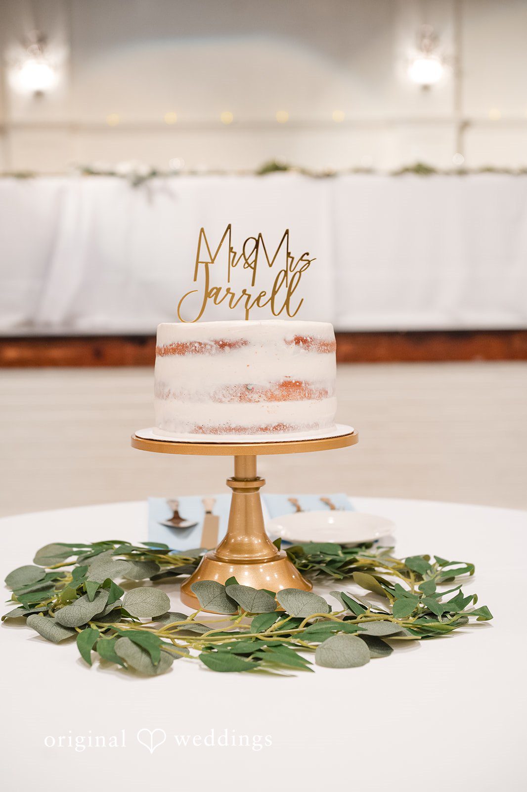 Jaclyn + Mason Multi-tiered white wedding cake decorated with green leaves.
