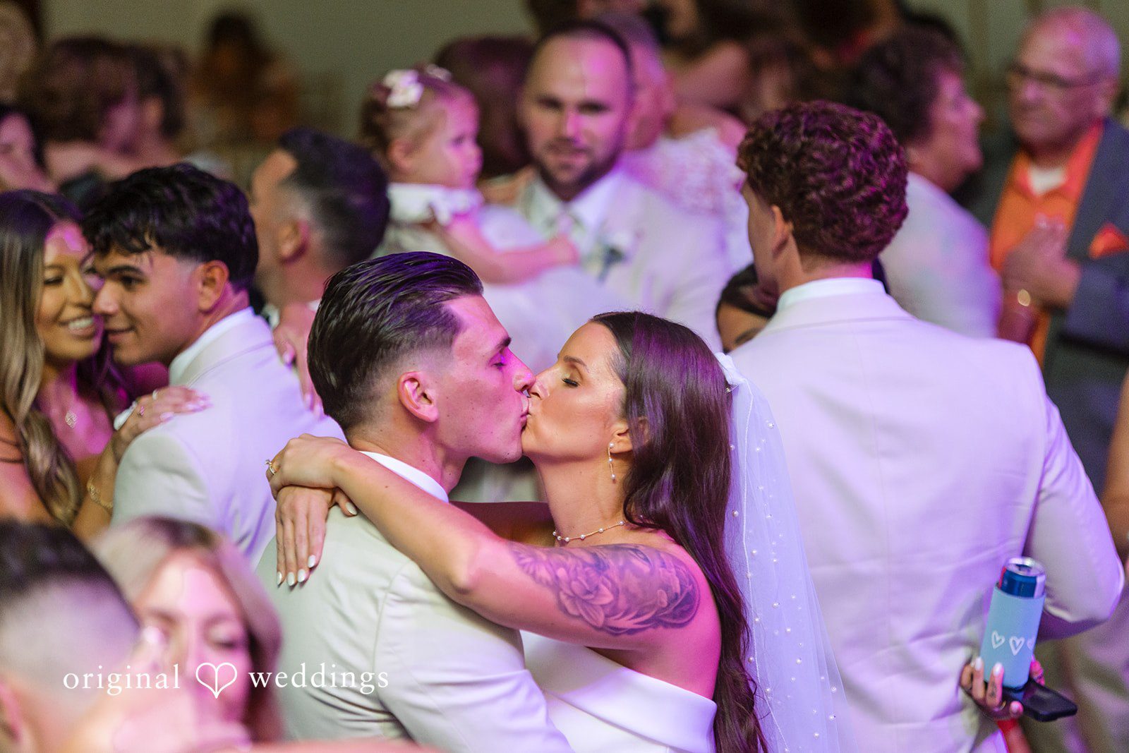 Jaclyn + Mason Bride and groom hugging and kissing surrounded by reception guests.
