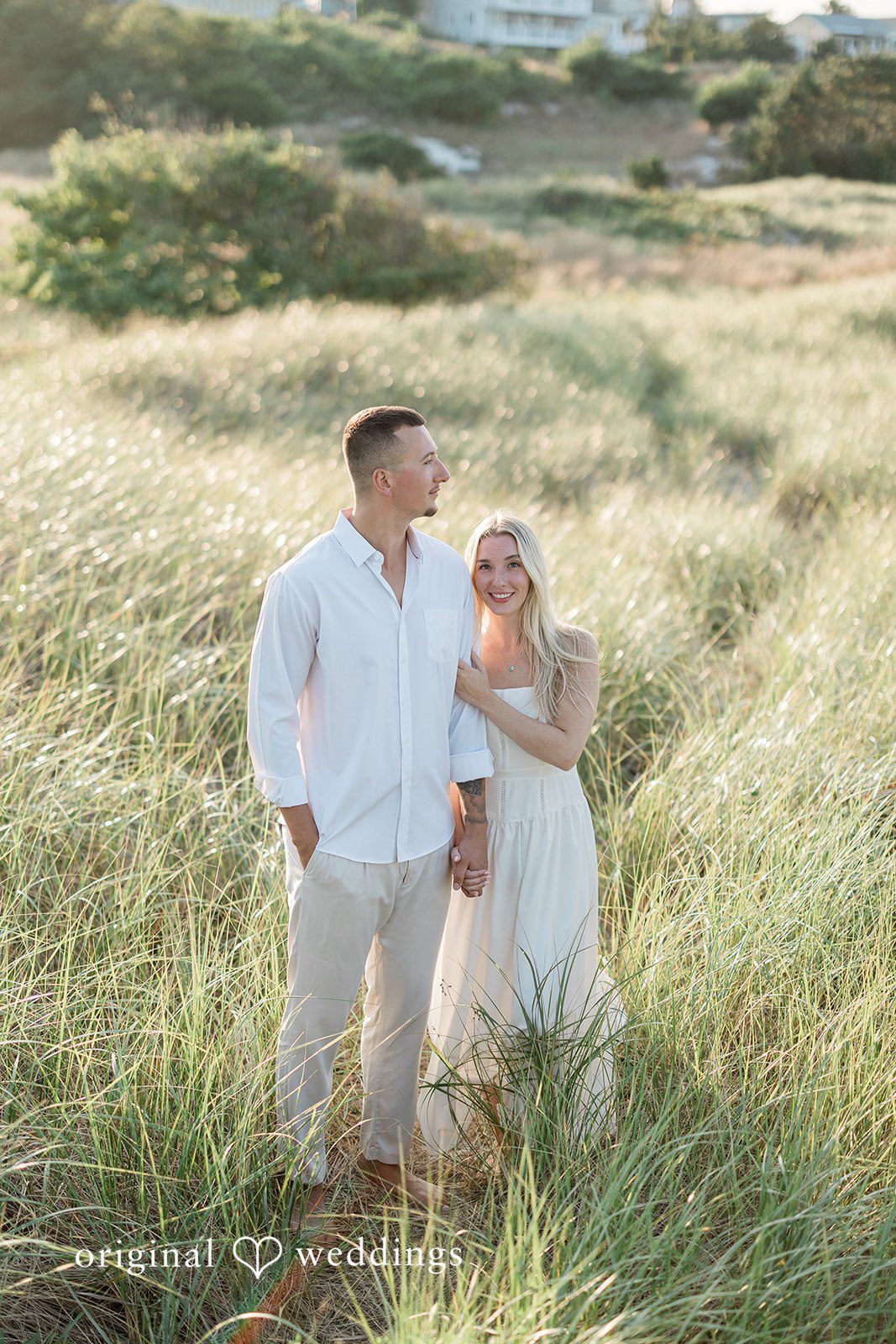 A wide shot of a couple standing together in a grassy field.