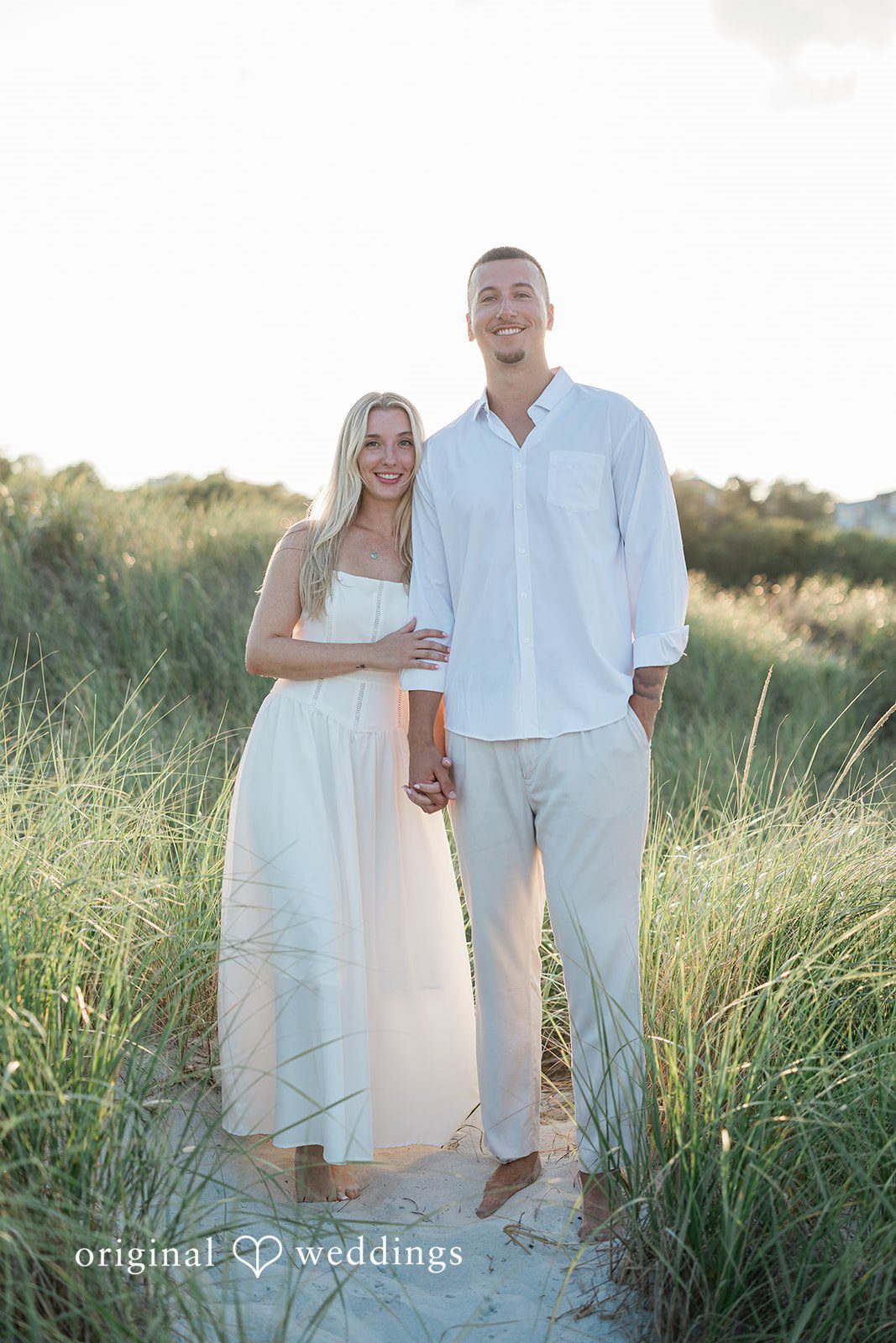 A couple standing close together in front of a grassy backdrop.