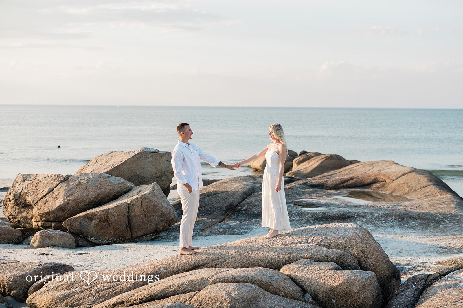 A distant shot of a couple standing on large coastal rocks.