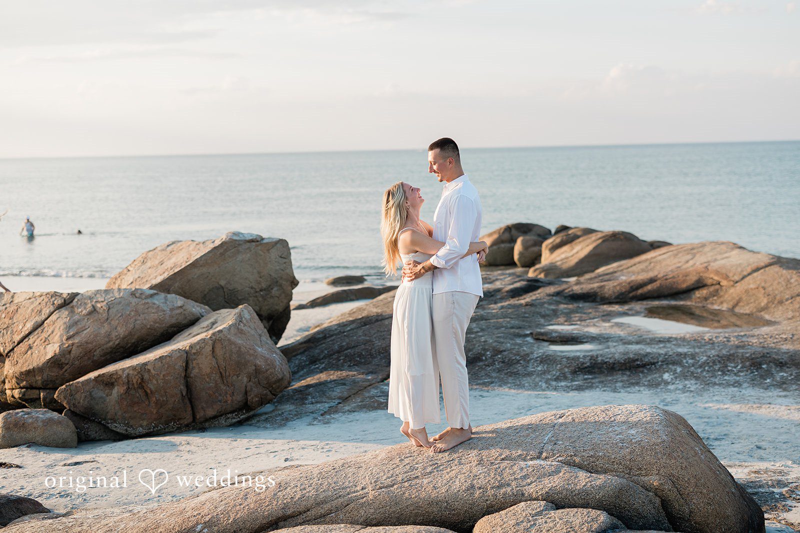 A couple standing together on a rocky shore looking out at the water.